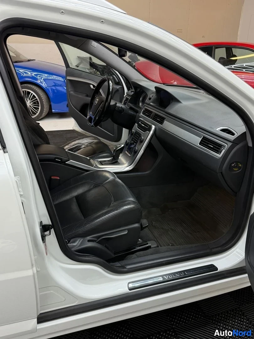 Muu: Ajoautoon avattu kuljettajan ovi paljastaa mustan nahkasisustuksen, Volvon ohjauspyörän ja keskitason; ovenlistassa Volvo-teksti.