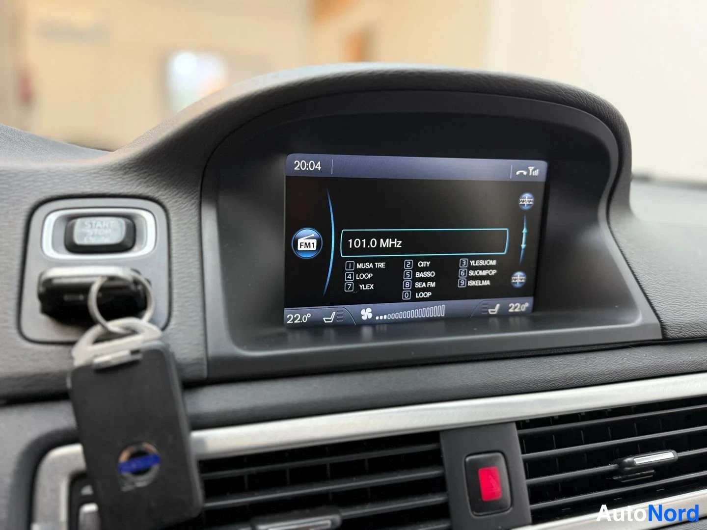 Muu: Volvo kojelaudan näyttö näyttää radiovastaanoton FM1 101.0 MHz; moottorin käynnistyspainike ja avaimet paneelissa.