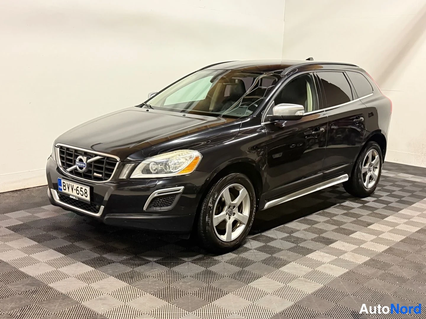 Etuviisto, nokka vasemmalle: Mustan Volvo XC60:n etu-kolmasosakuva sisätiloissa, keula vasemmalla.