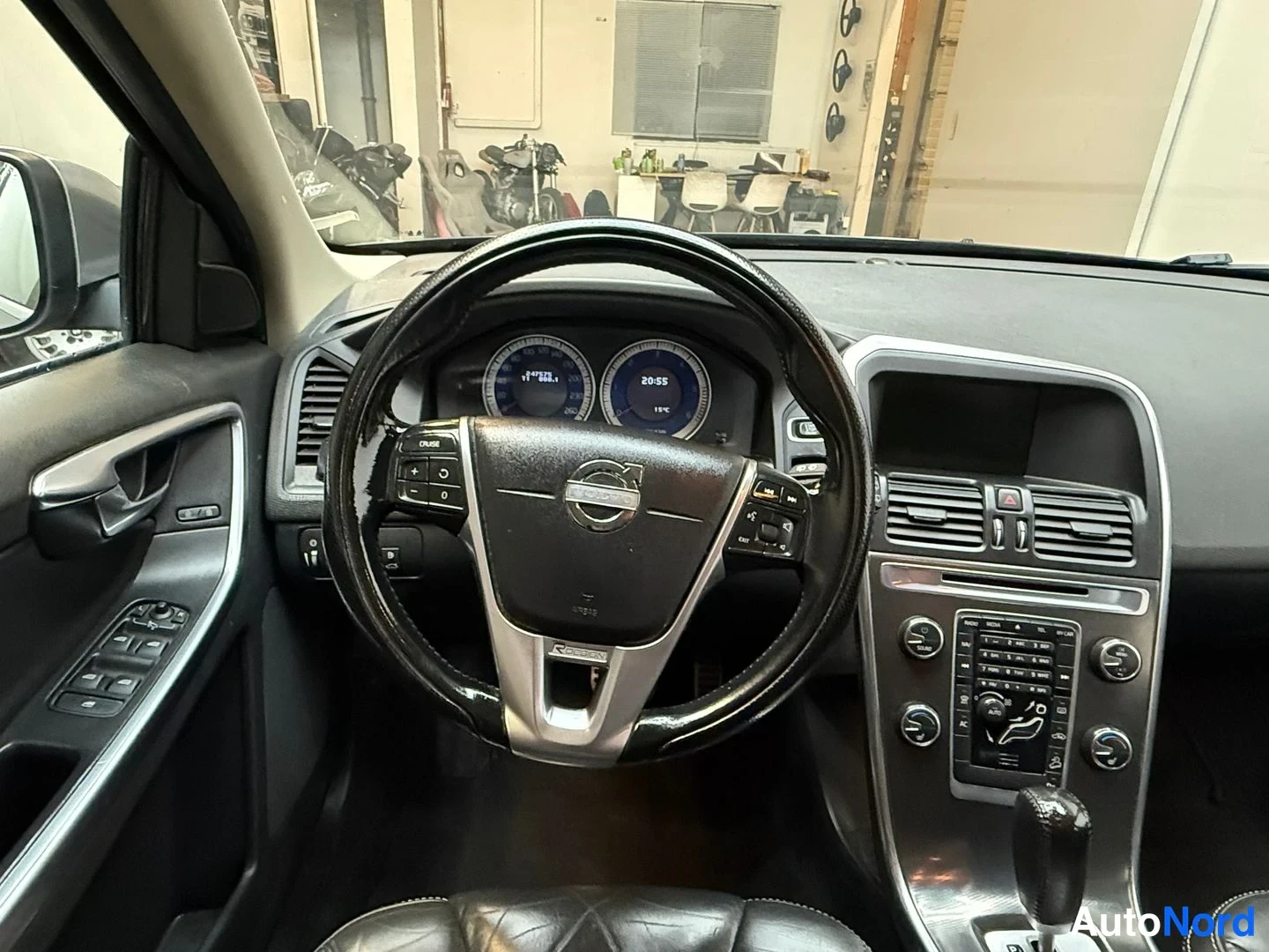 Edestä: Ohjauspyörän tarkempi kuva: Volvo-merkki, R-Design-teksti ja mittaristo, kojelaudan säätimet ja vaihtaja.