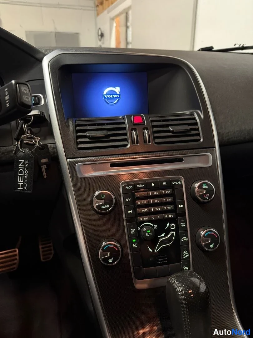 Muu: Auton kojelaudan keskikonsoli: näytössä Volvo-logotunnus, radio- ja ilmastointipainikkeet sekä avaimet riippuvatvirtaimet HEDIN AUTOMOTIVE -avainnauhalla.