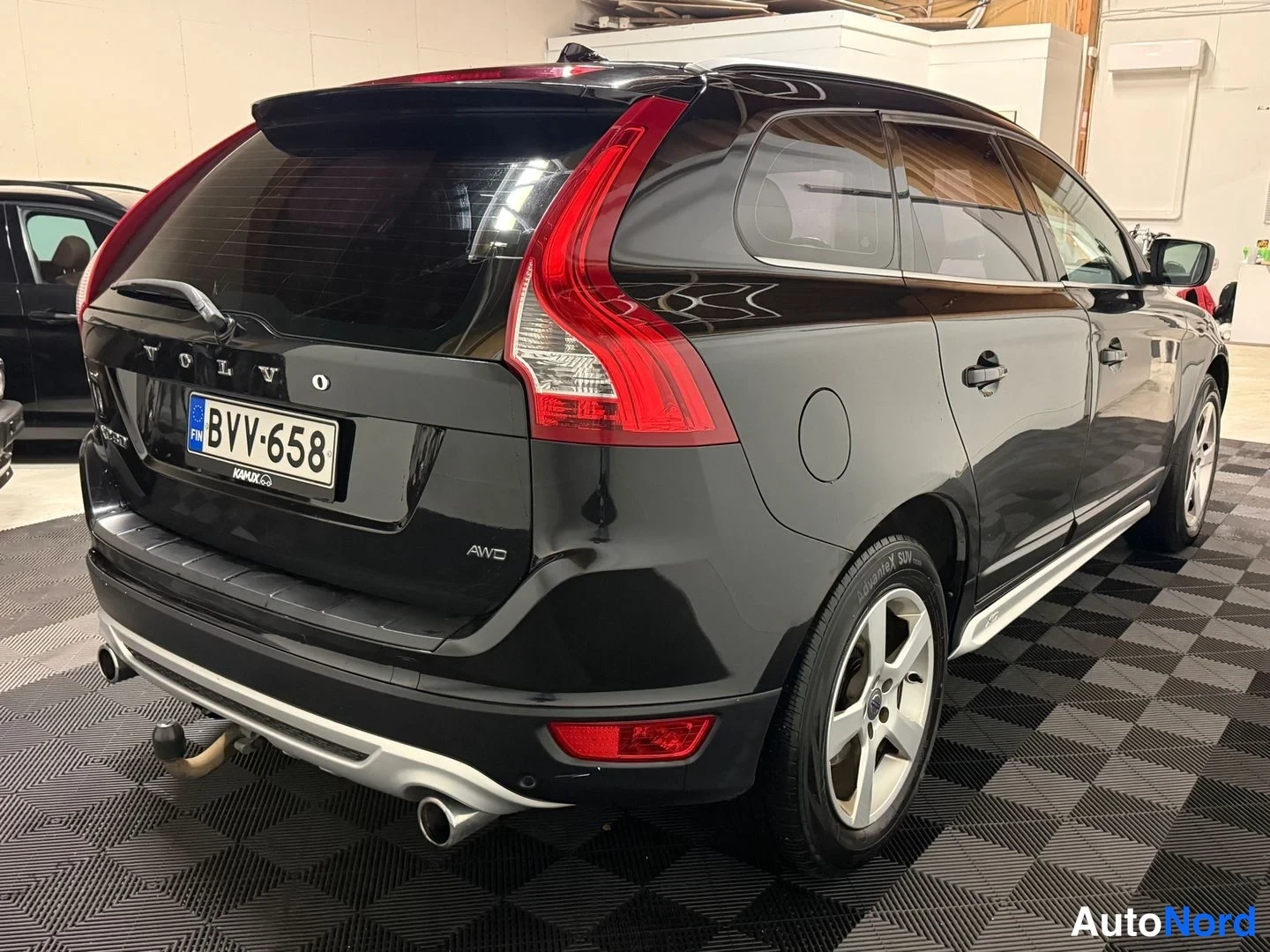 Takaviisto: Mustan tila-auton takaosa ja kylki kolmasosakulmassa: rekisteri, VOLVO-teksti takaluukussa, AWD-tarra, hinauskoukku ja kromilistat.