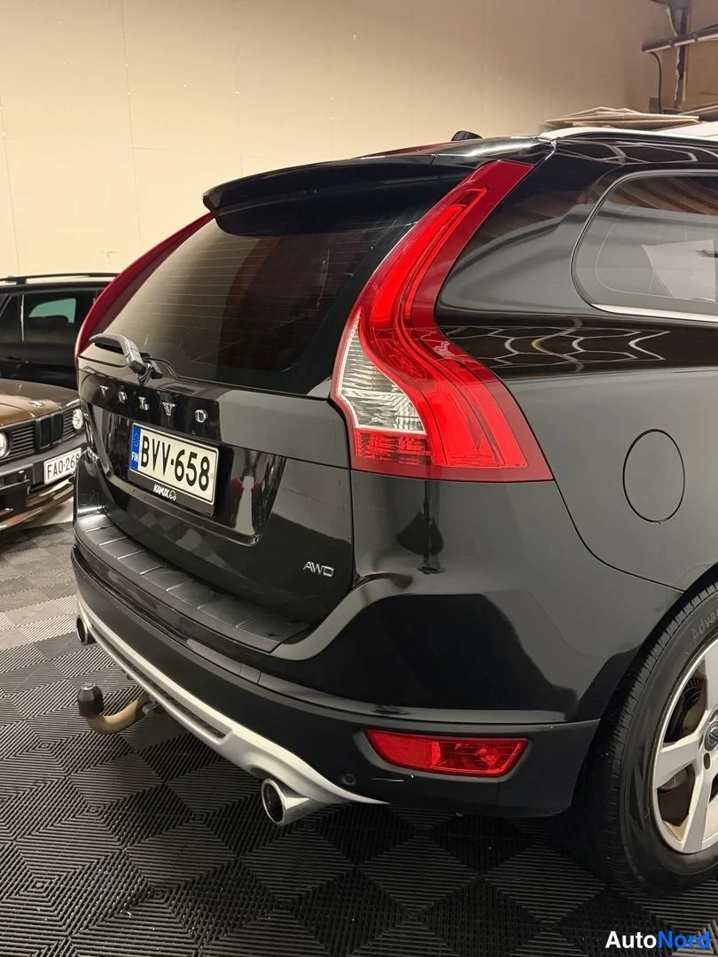 Takaviisto: Mustan tila-auton takaosa lähikuvassa: VOLVO-merkki, rekisteri, AWD-tarra, hinauskoukku ja kromipuskurisuoja.