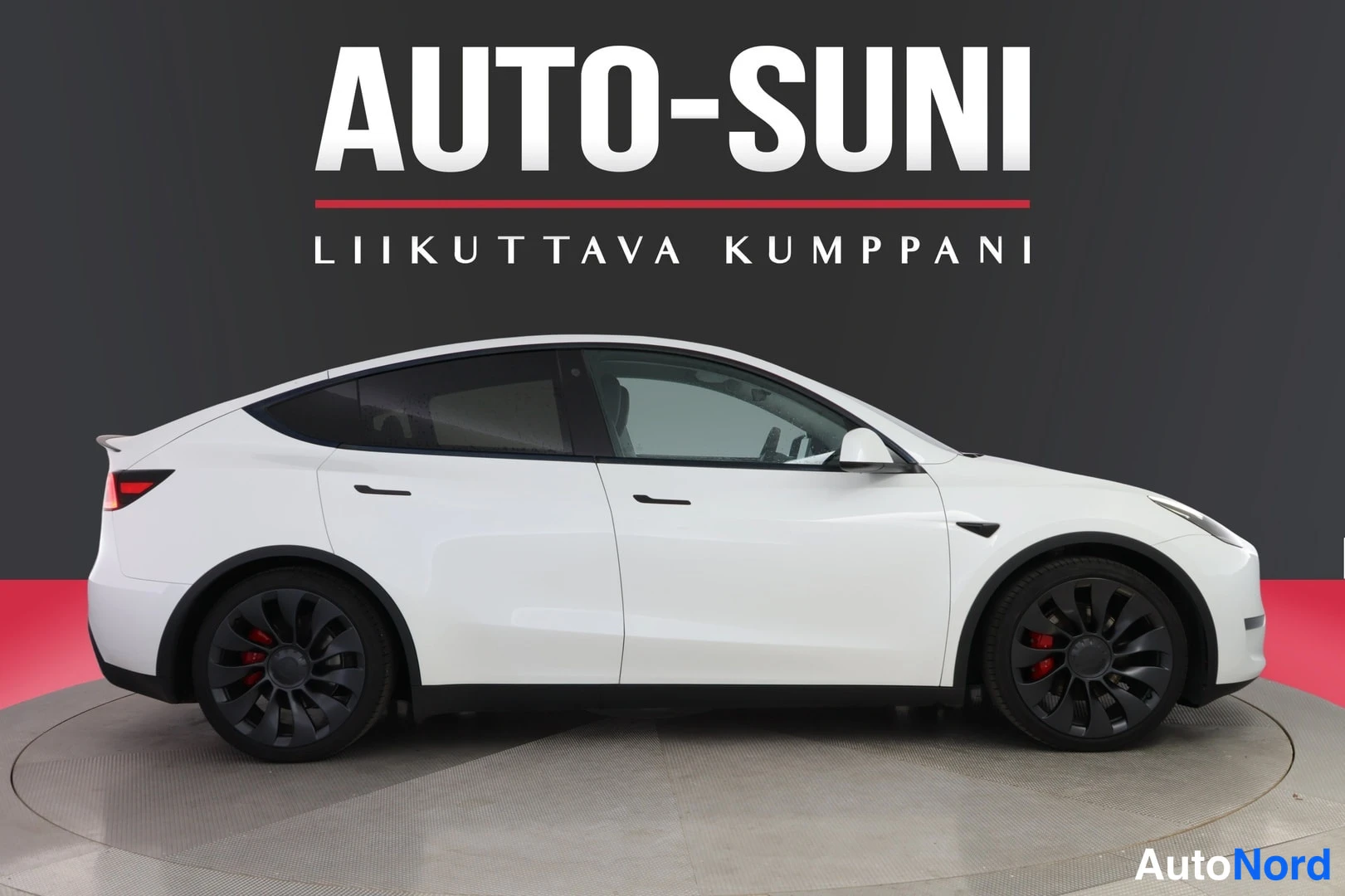 Sivulta: Valkoinen Tesla Model Y sivukulmassa, mustat vanteet punaisilla jarrusatulolla.