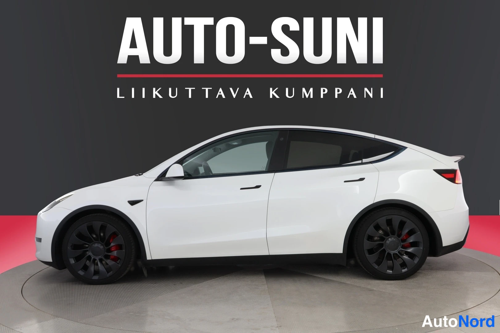 Sivulta: Valkoisen Tesla Model Y -farmarin sivuprofiili studioissa, tummat kevytmetallivanteet ja punaiset jarrusatulat näkyvät.