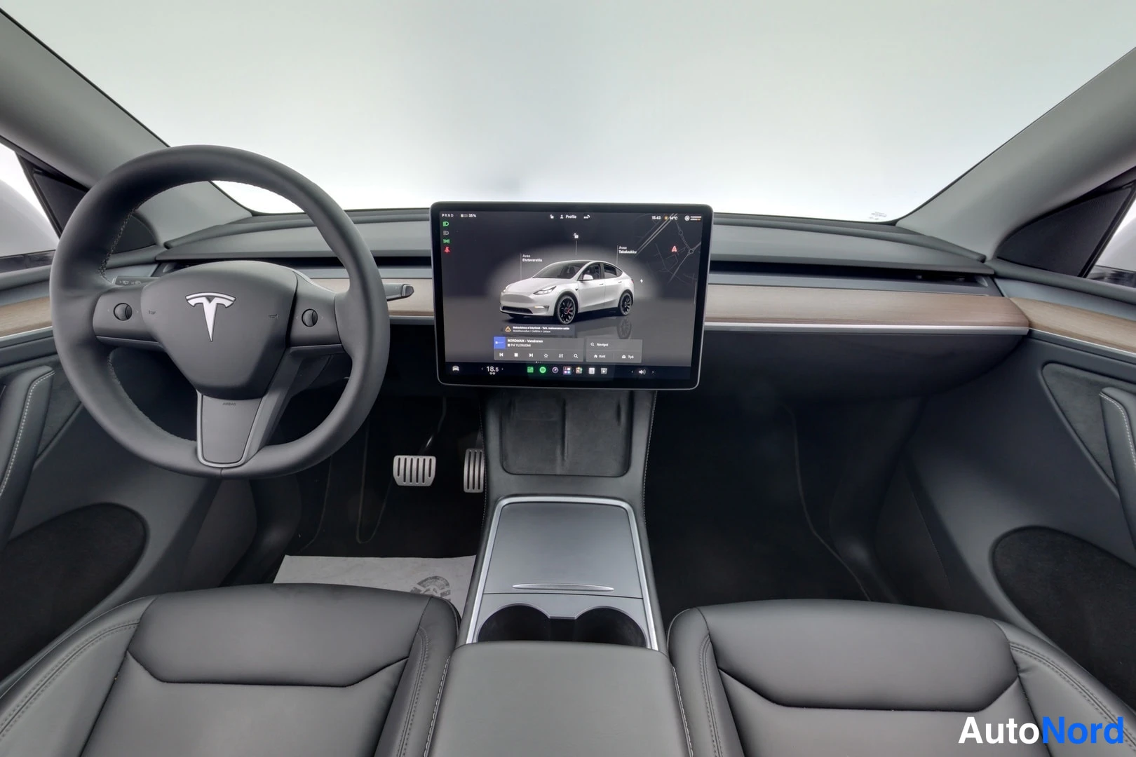 Muu: Tesla Model Y:n etuohjaamo: ohjauspyörä, puusomisteinen kojelauta ja suuri keskellä oleva kosketusnäyttö.