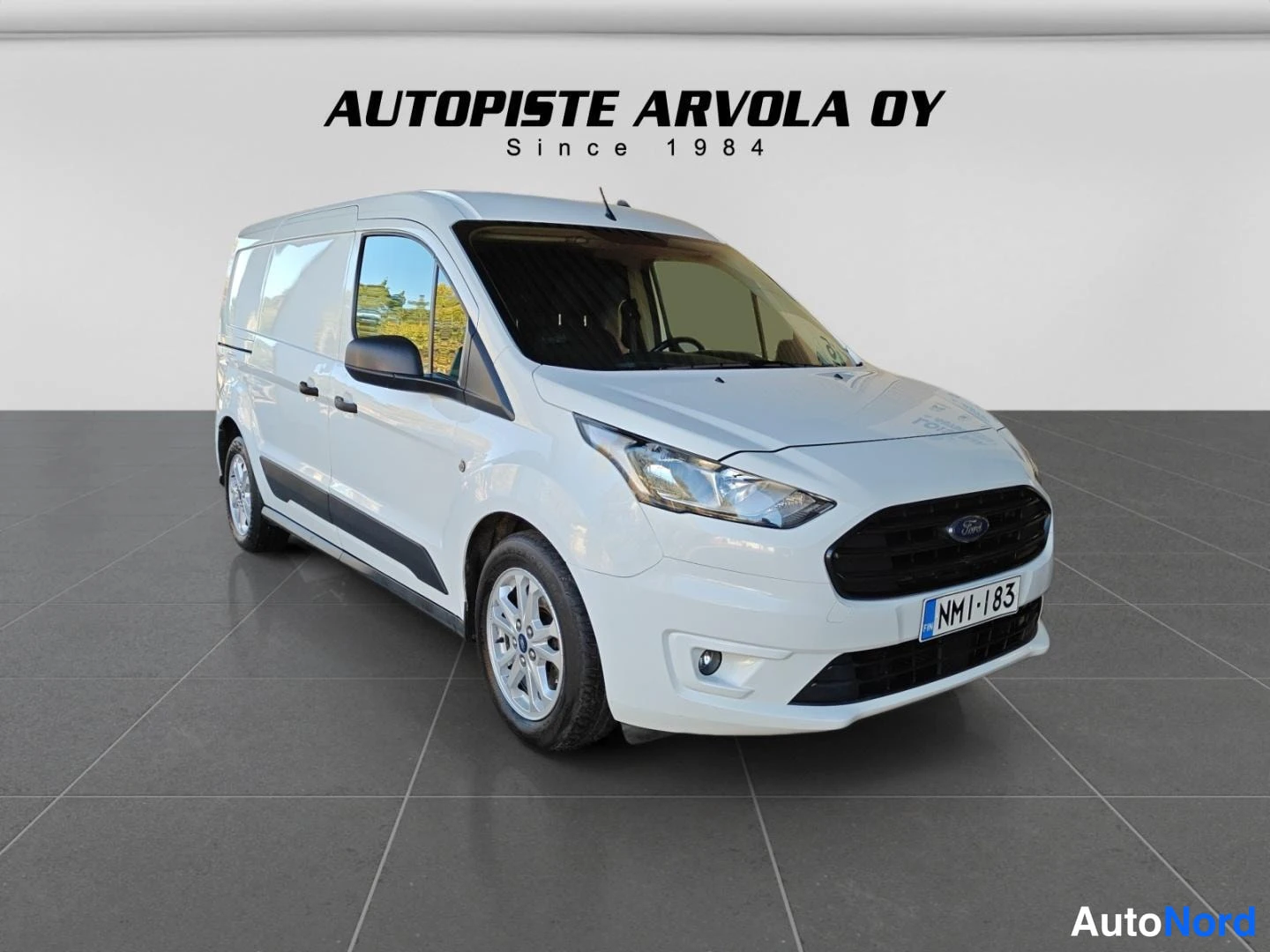 Etuviisto, nokka oikealle: Valkoinen Ford Transit Connect -pakettiauto kolmesta neljännesnäkymästä edestä, keulan osoitteessa oikealle; rekisterikilpi NM1-183.