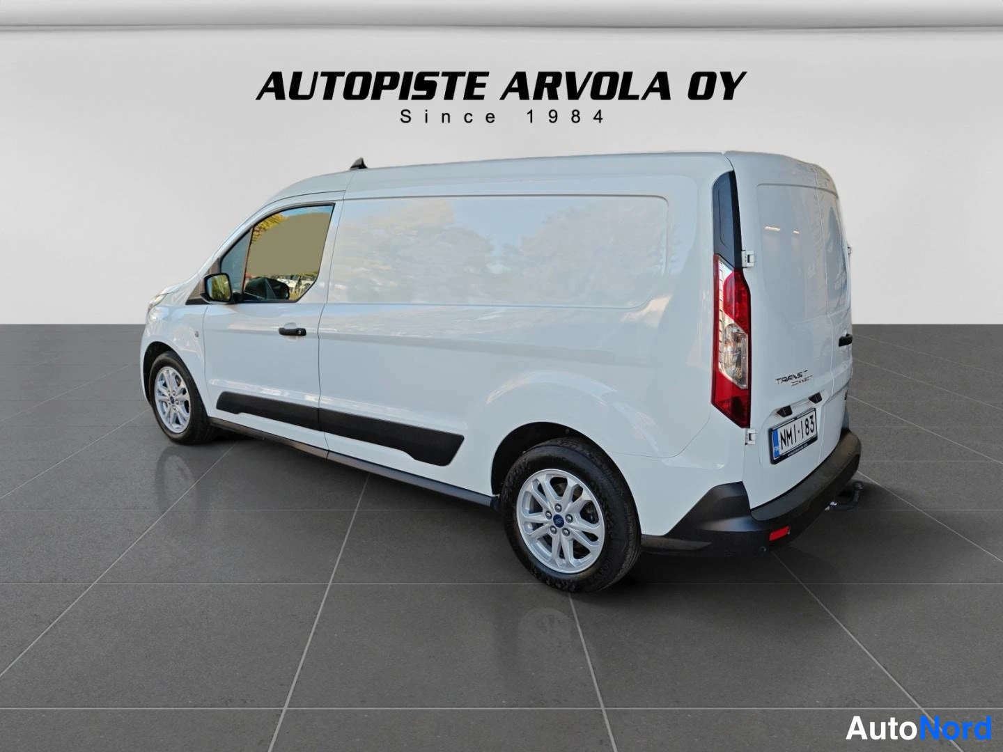 Takaviisto: Valkoisen Ford Transit Connect -pakettiauton takaosa ja vasen kylki kolmasosakulmassa, taustalla studiovaalea seinä.