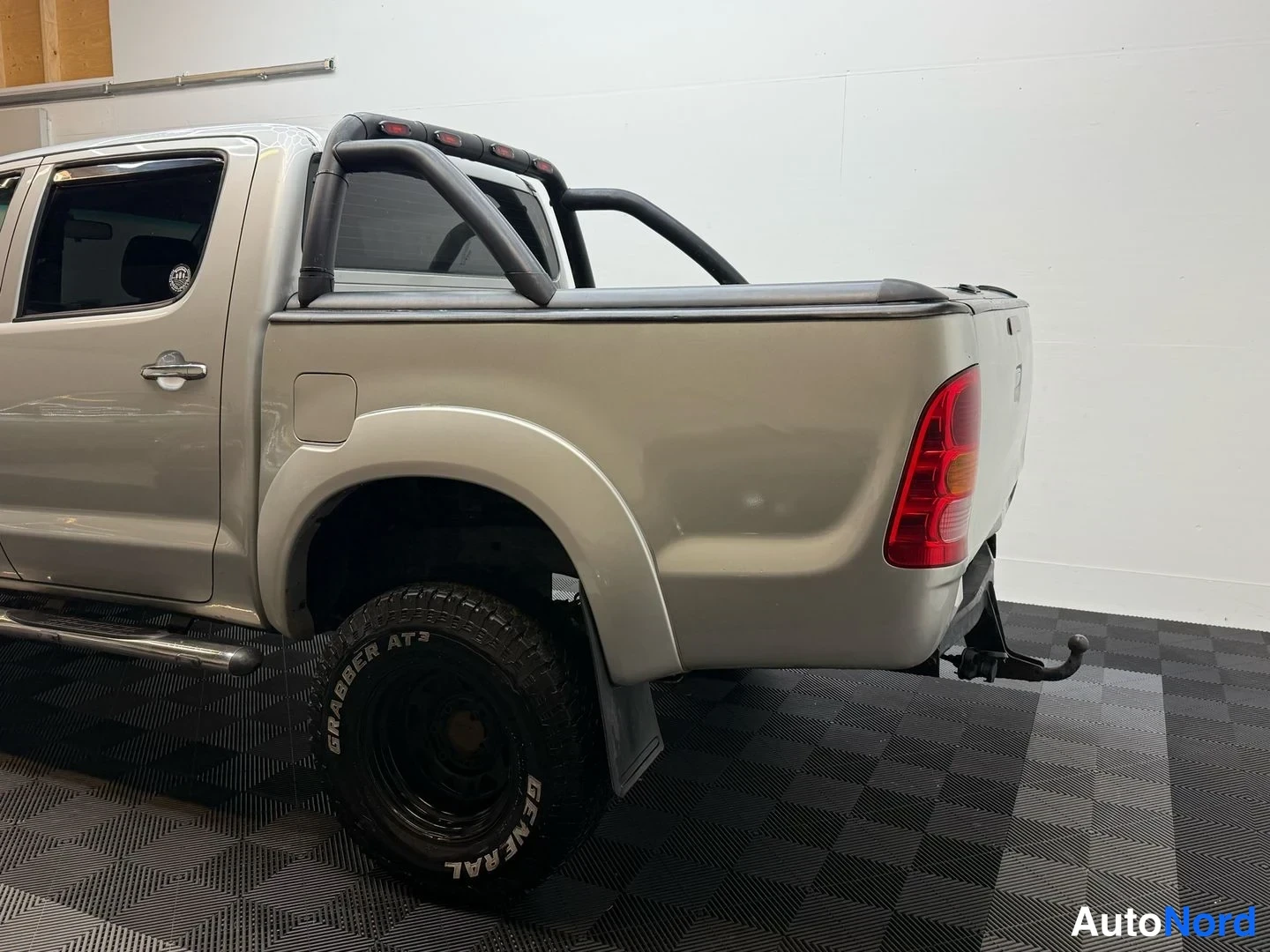 Takaviisto: Toyota Hilux -avolavan takakulma: black tonneau cover, roll bar and tow hook visible