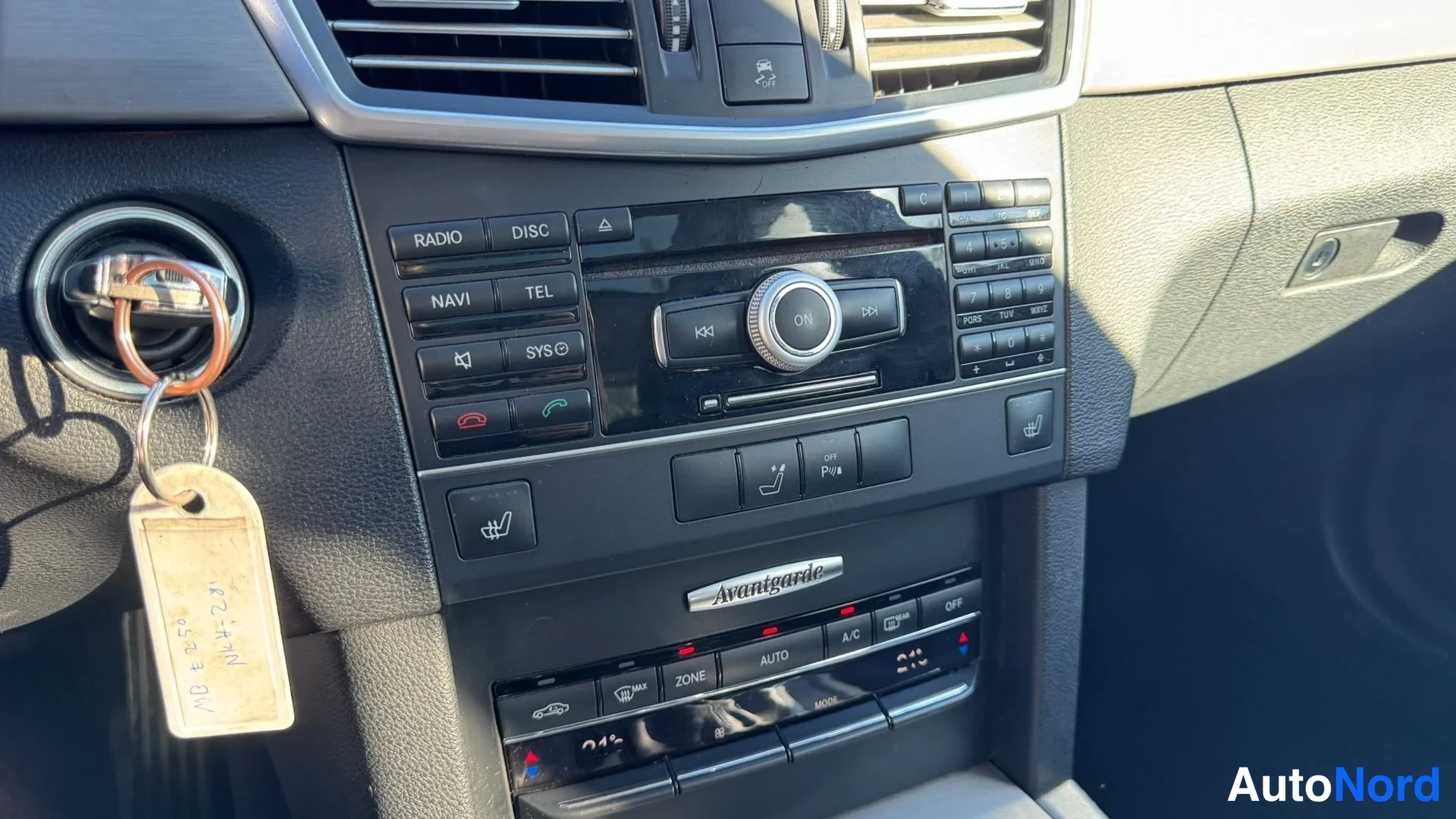 Yksityiskohta: Keskikonsolin radio- ja ilmastointipaneeli, jossa näppäimet RADIO, DISC, NAVI, TEL, sytytysavaimet ja Avantgarde-teksti. Ilmastointi näyttää 21°C ja AUTO.