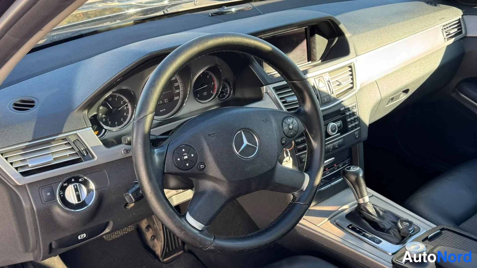 Yksityiskohta: Ohjaamon näkymä: Mercedes-ohjauspyörä, analogiset mittarit, keskikonsoli ja automaattivaihteen valitsin.