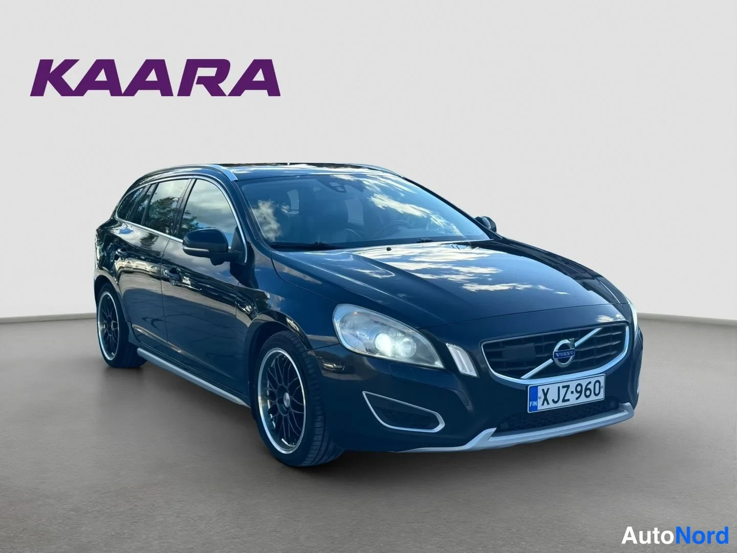 Etuviisto, nokka oikealle: Musta farmariauto, Volvo V60, edestä oikealta kuvattuna studiotaustaa vasten.