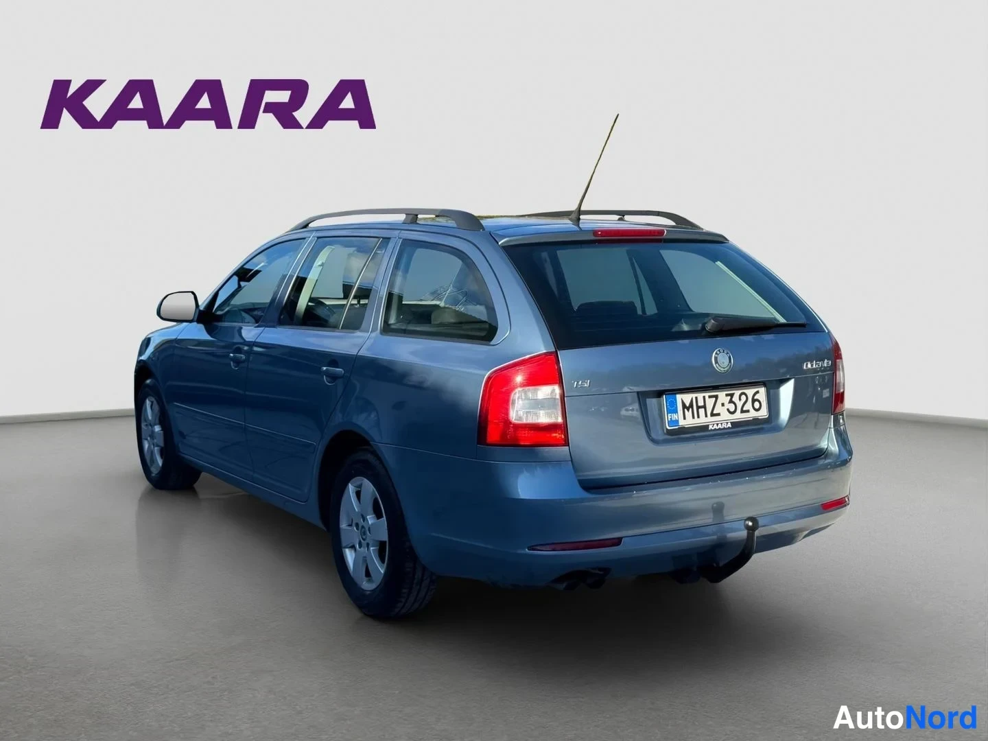 Takaviisto: Sininen Skoda Octavia Combi -farmari takaa ja vasemmalta sivulta kuvattuna, rekisteritunnus, kattokaiteet ja vetokoukku näkyvissä.
