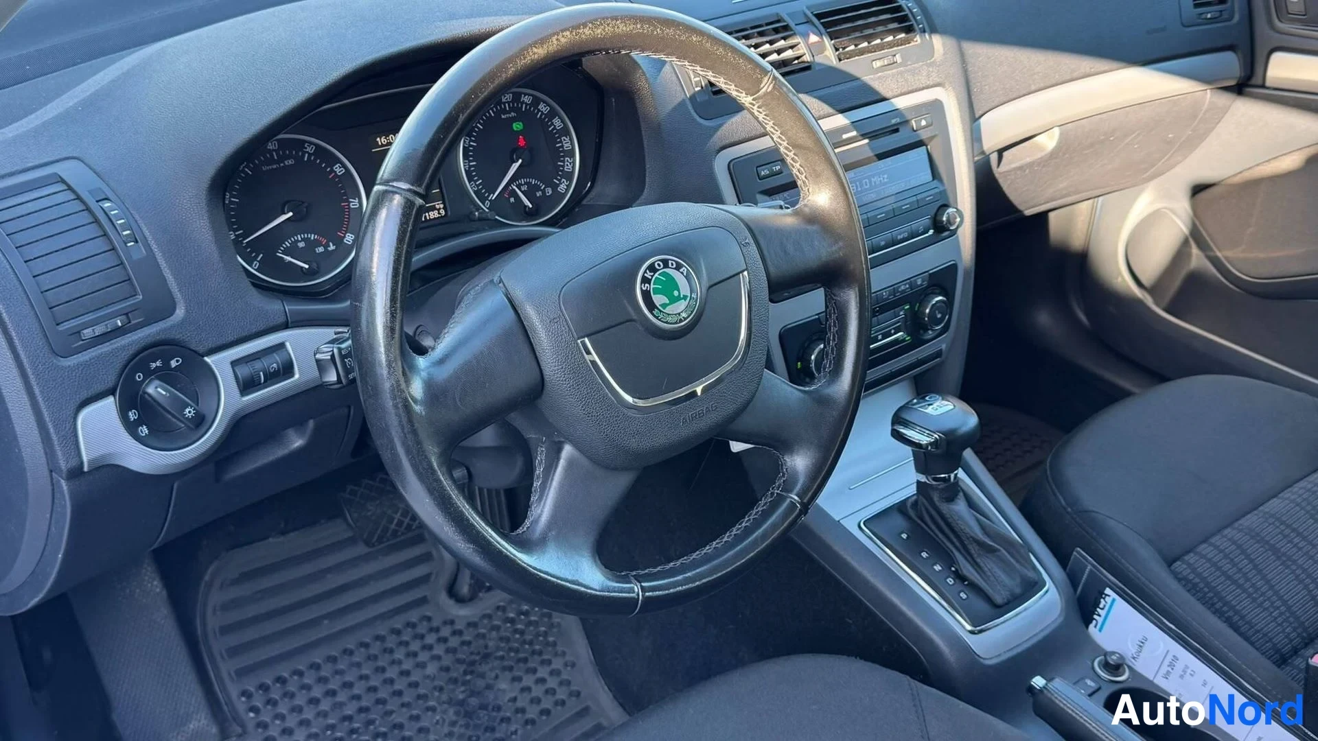 Muu: Ohjaamon näkymä: Škoda-merkkinen ohjauspyörä, analogiset mittarit, automaattivaihteen valitsin ja kojelaudan keskikäyttöpaneeli.