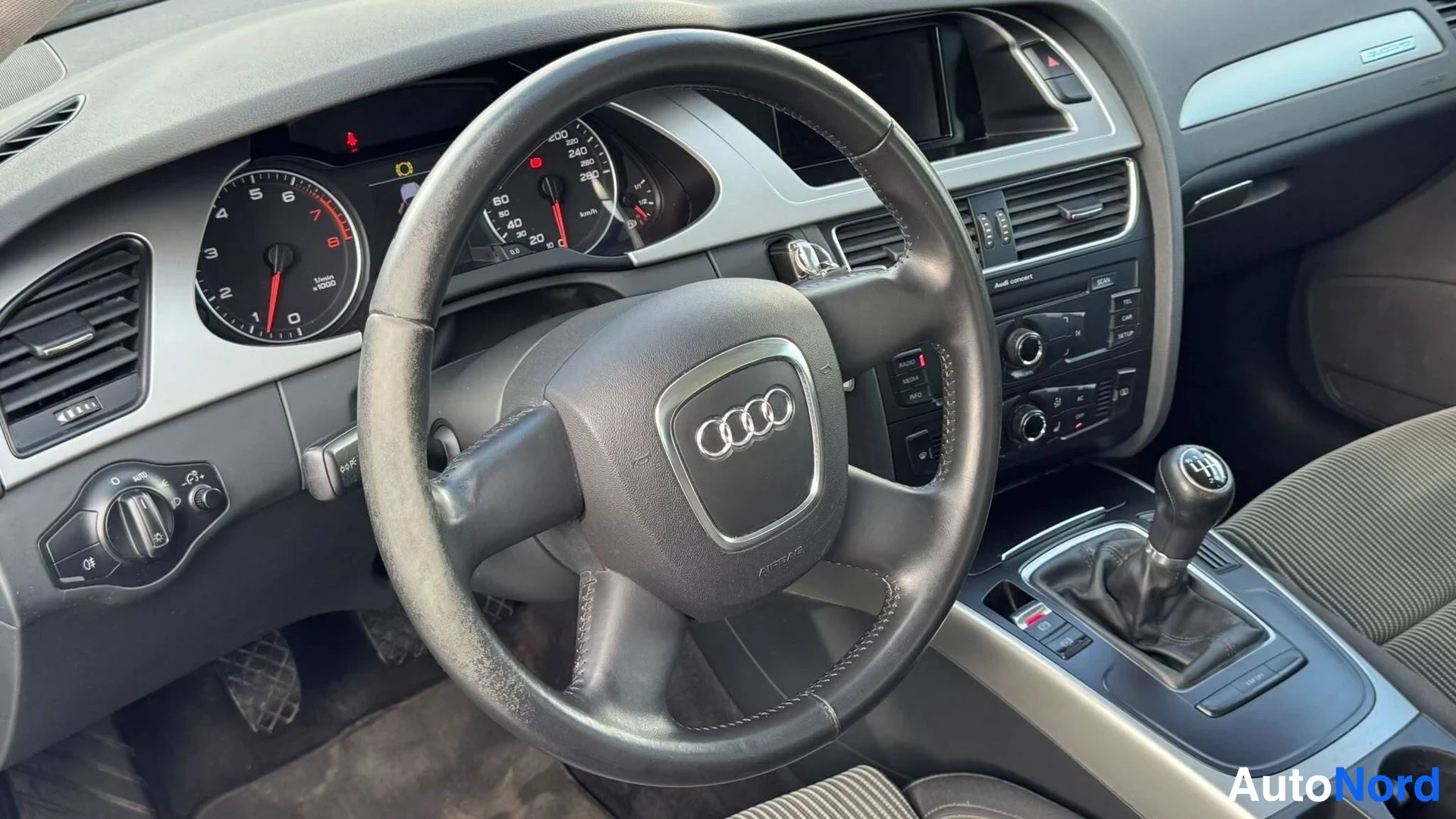 Edestä: Interiöörin kojelauta ja ratin kojelaudan mittaristo, manuaalivaihteistossa näkyy vaihdin, käsijarru ja Audi-Logo ratti