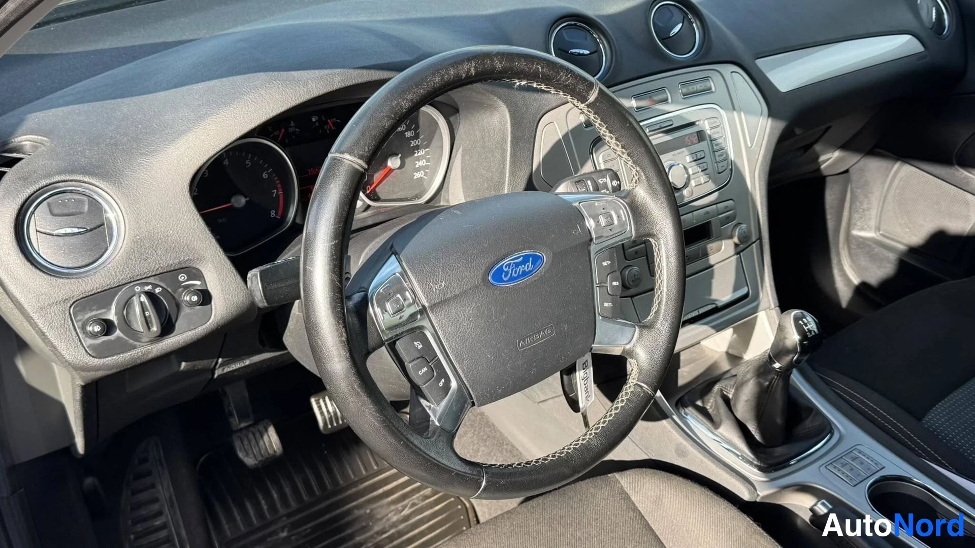 Muu: Ford Mondeon ohjaamo: ratin Ford-merkki, mittaristo, manuaalivaihtoaita ja keskinäiskonsoli.