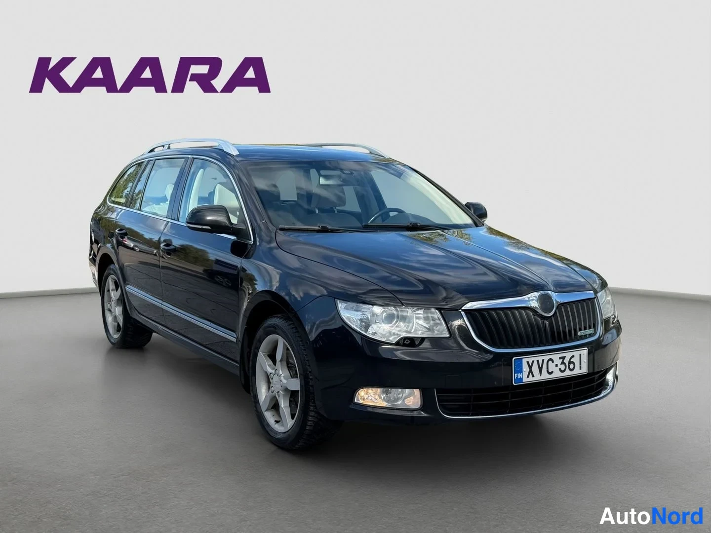Etuviisto, nokka oikealle: Tummansininen Skoda Superb Combi kolmen neljännes etunäkymässä oikeasta etukulmasta, katolla kattotelineet, rekisterikilpi.