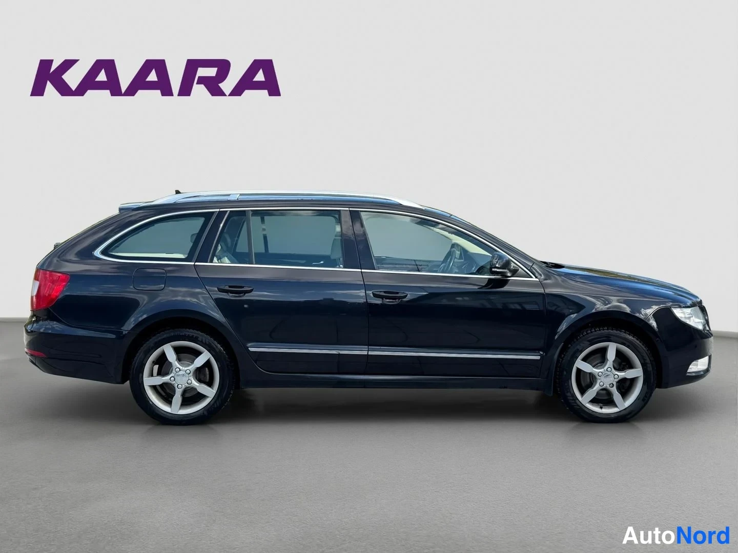 Sivulta: Sivunäkymä tummansinisestä Skoda Superb Combi -asema-autosta, vasen sivu kokonaan näkyvissä viidellä pistoraisella ja hopeisilla vanteilla.