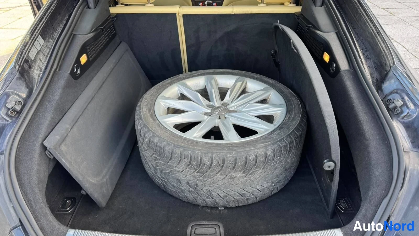 Muu: Auton avattu tavaratila, jonka lattialla on vararengas hopeapohjaisella Audi-kevytmetallivanteella talvirenkaalla; tavaratilan sivupaneelit ja verhot irrotettun