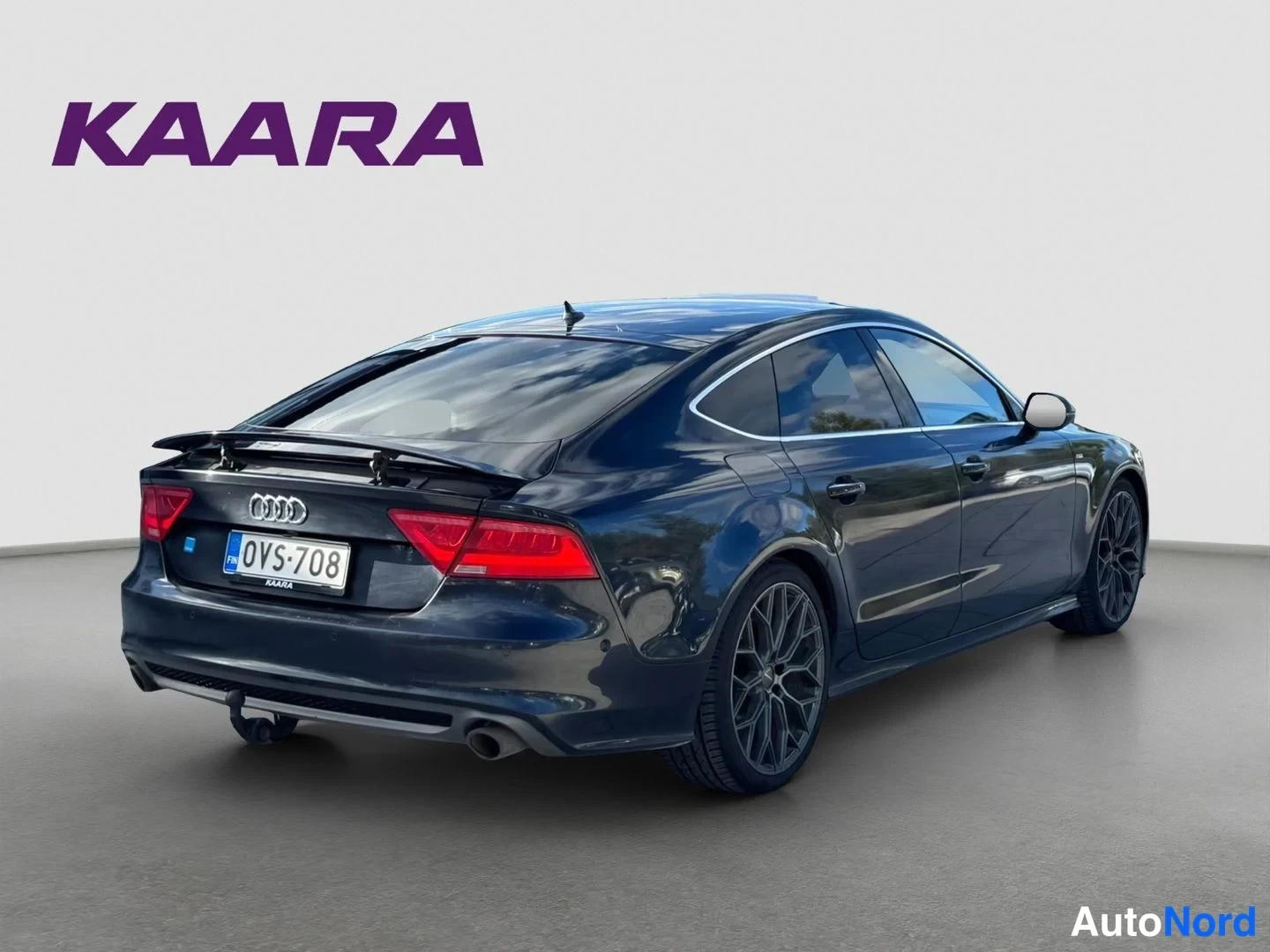Takaviisto: Audi A7 -auto tummansinisenä taksakulmasta oikealle, rekisteritunnus, vetokoulu ja kattospoileri näkyvissä.