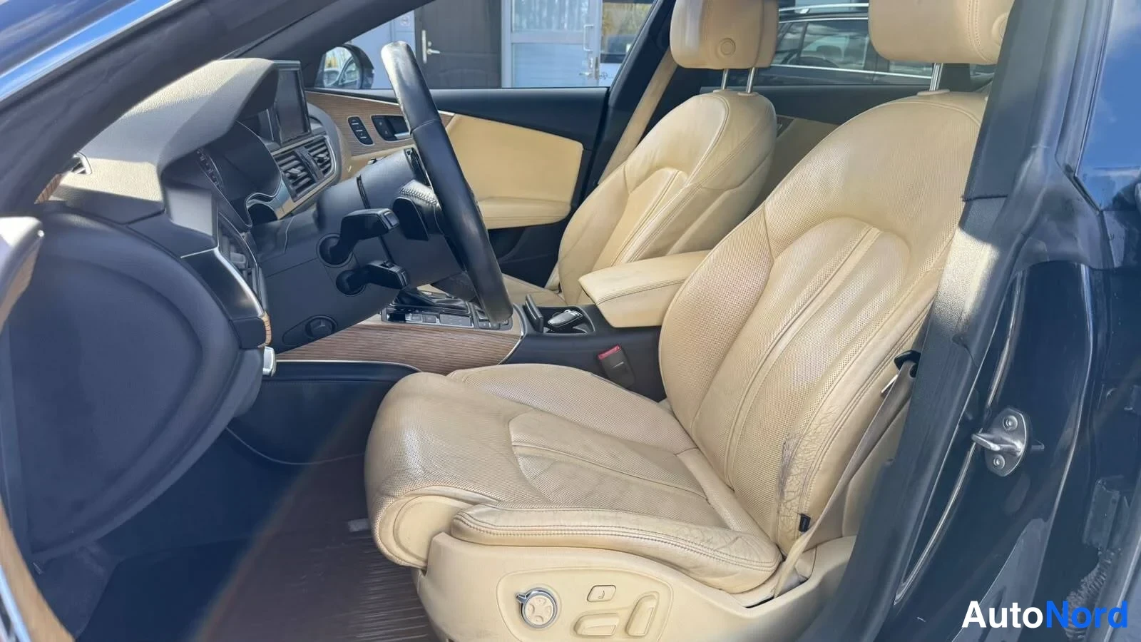 Etuviisto: Audi A7:n etumatkustustila sivulta kuvattuna: kaksi vaaleanruskeaa nahkaistuinta, keskikonsoli ja nahkaverhoiltu ohjauspyörä.