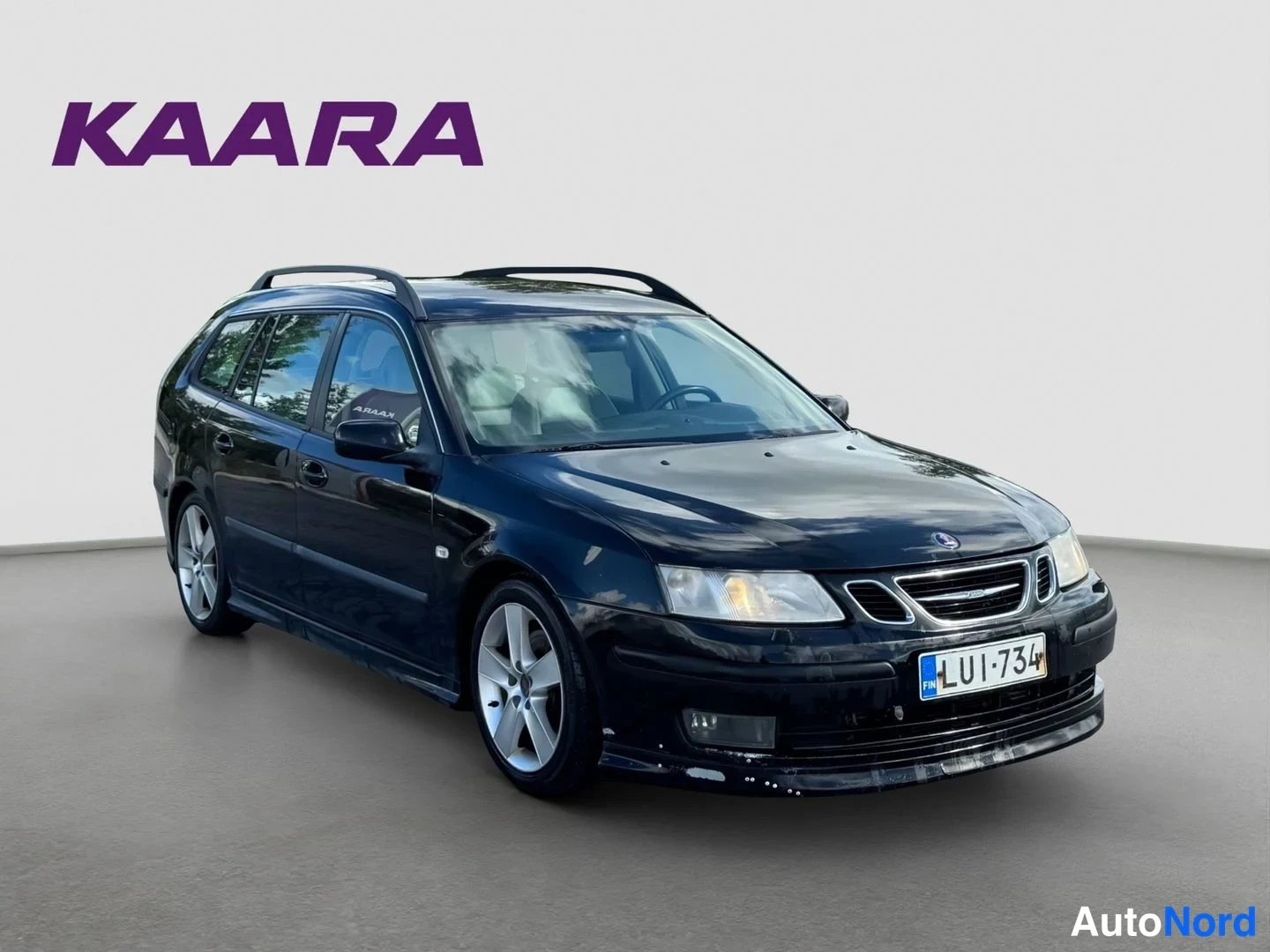 Etuviisto, nokka oikealle: Musta Saab 9-3 SportCombi etuosasta oikealta kolmemmelta suunnalta, rekisteritunnus, sumuvalot ja kattokaiteet näkyvissä.