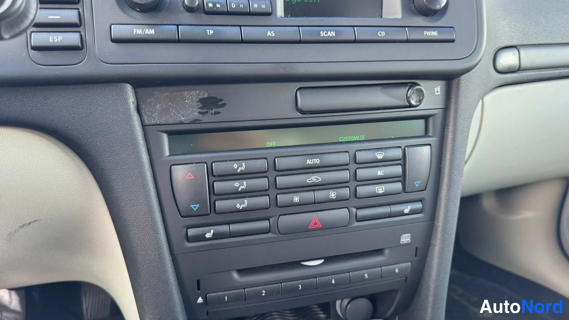 Muu: Ilmastoinnin automaattiohjain keskikonsolissa: AUTO-, AC- ja istuimenlämmitysnäppäimet, kolmen numeroitu säätönappi, varoitusvalon kolmio ja CD-lukija.