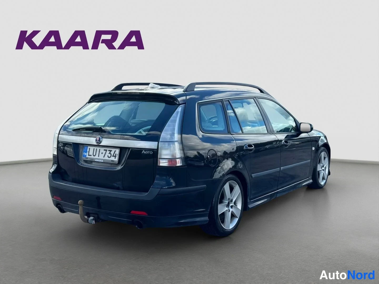 Takaviisto: Musta Saab 9-3 SportCombi takaa oikealta kolmemmelta suunnalta, rekisteritunnus, kattokaiteet ja takana vetokoukun kaula näkyvissä.