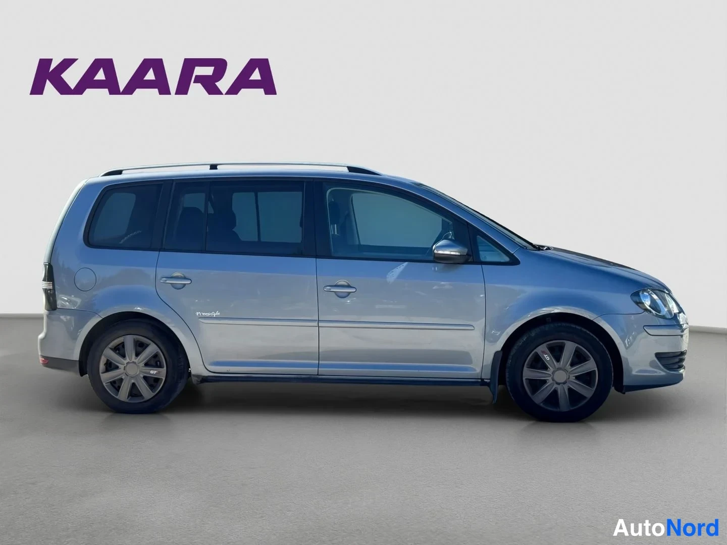 Sivulta: Hopeanharmaa Volkswagen Touran sivulta vasemmalta, kattokaiteet ja pyörät näkyvissä.