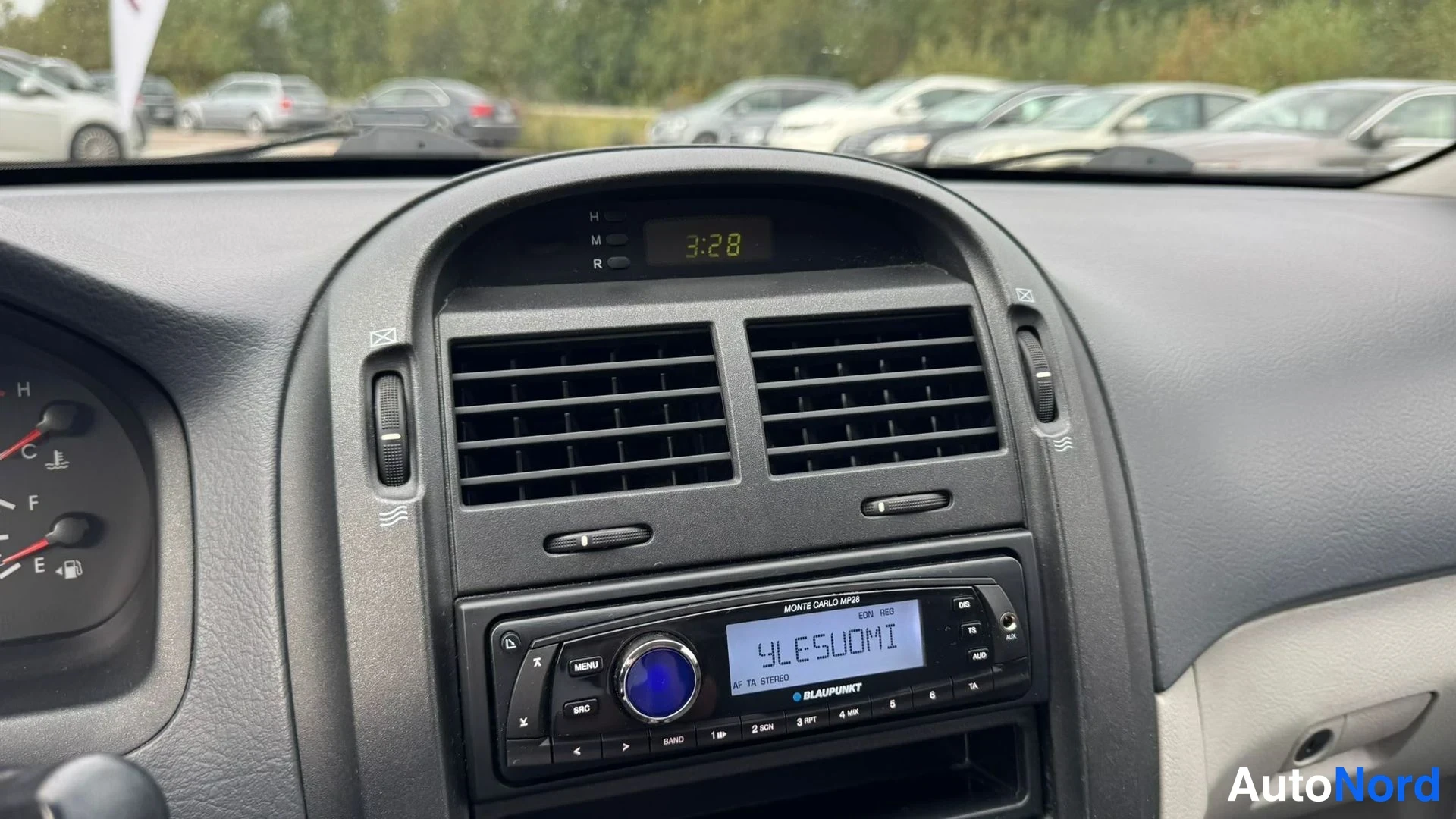 Muu: Kojelaudan keskusta: digitaalinen kello näyttää 3:28, kaksi ilmastointiritilää ja Blaupunkt-radio, jonka näytöllä lukee YLESUOMI.