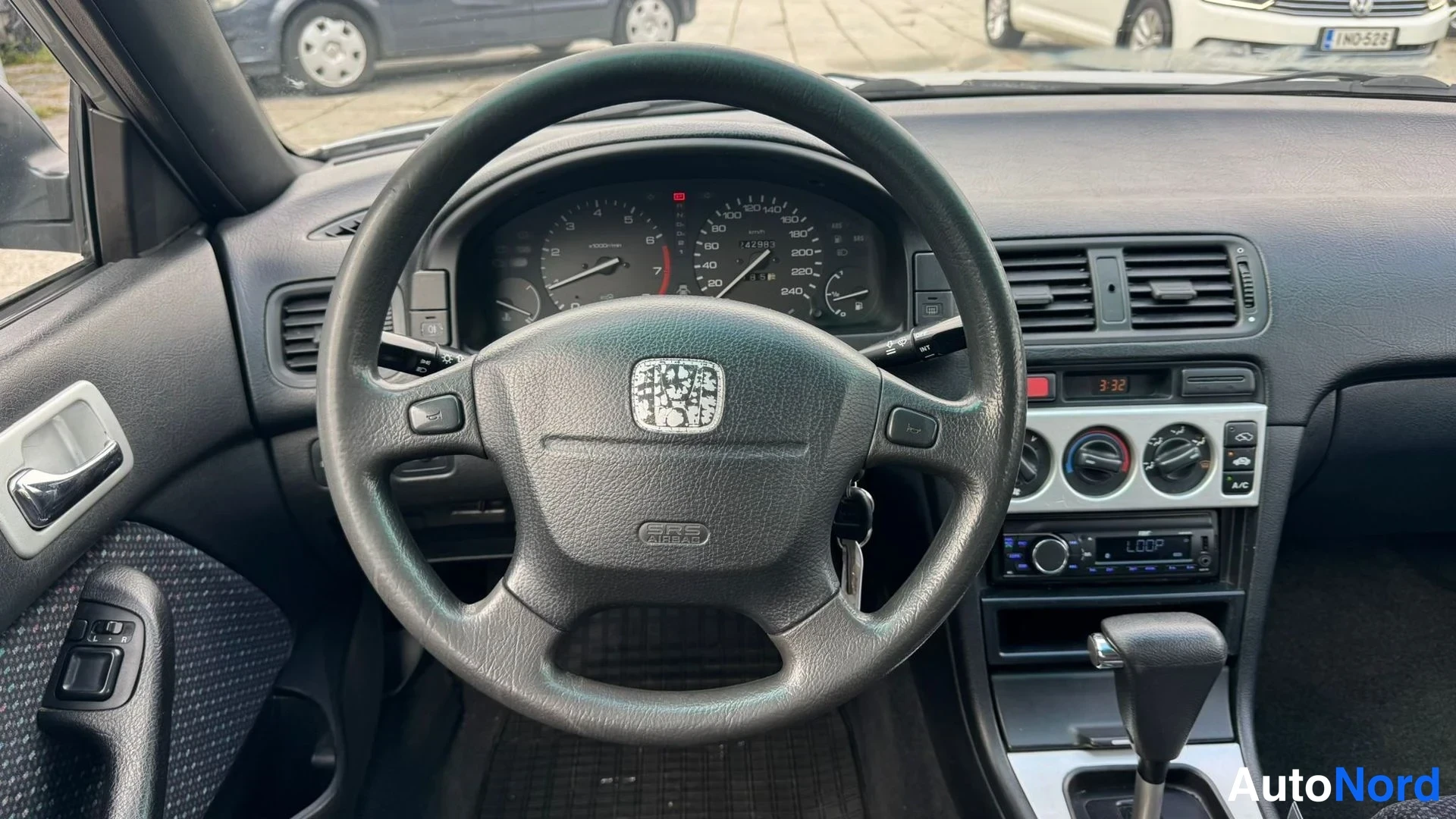Muu: Ohjauspyörä ja kojelauta lähikuvassa: Honda-merkki, mittaristo, SRS-tunnus ohjauspyörässä, radio ja automaattivaihteen valitsin.