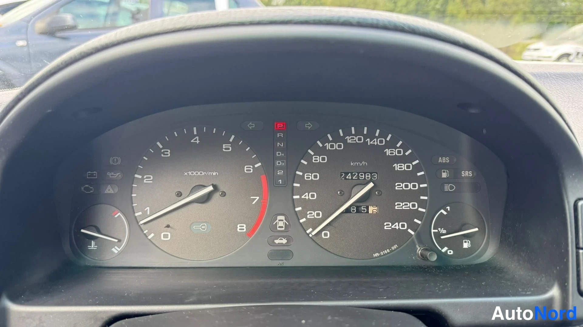 Muu: Mittaristo lähikuvassa: nopeusmittari näyttää lukemaa 242983 km, kierroslukumittari, ABS- ja SRS-symbolit sekä vaihdelaatikon R N D -asemat.