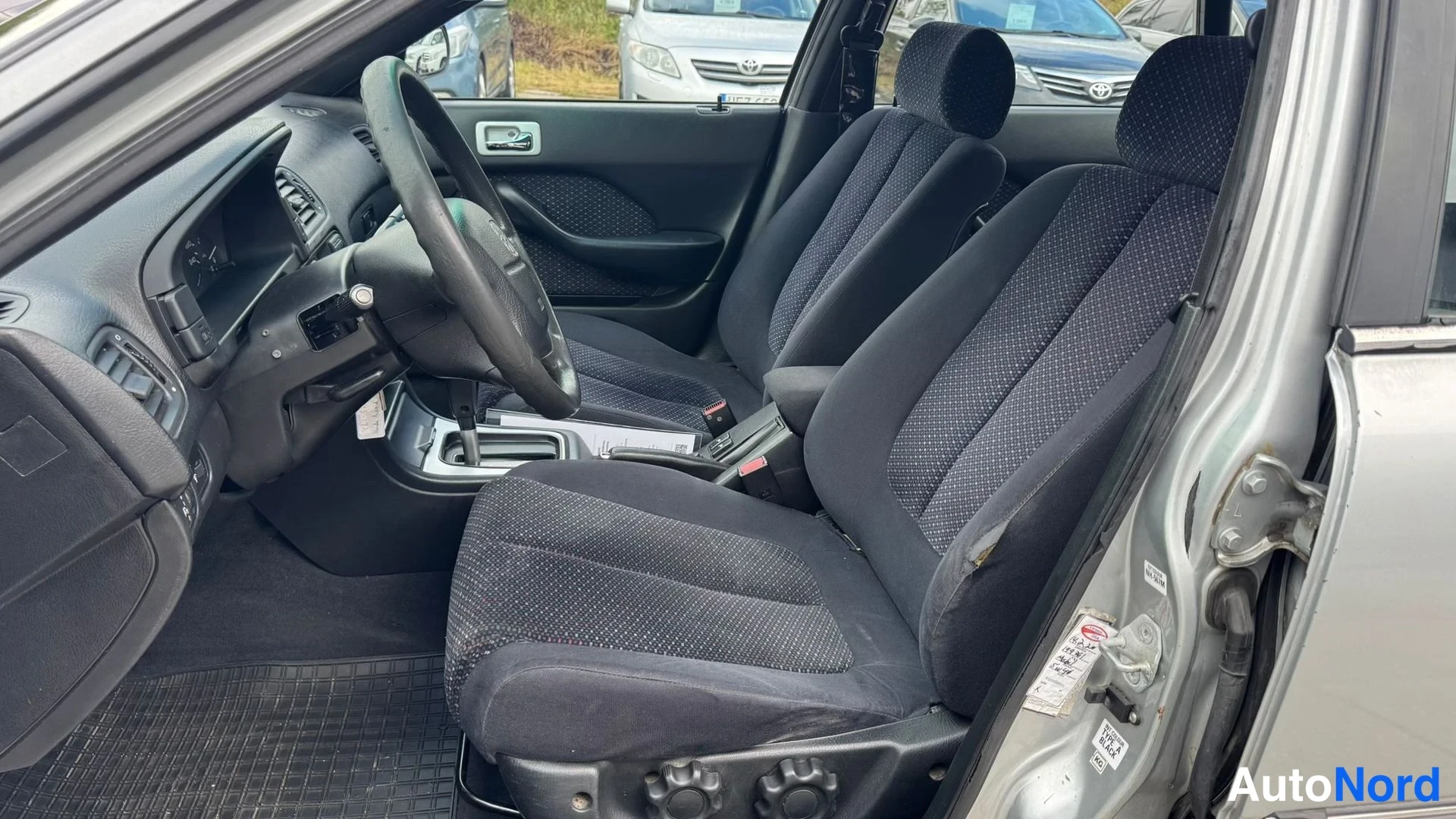 Etuviisto: Kuljettajan ovi auki kuvattu Honda Accordin sisätila: tummat kangasistuimet, ohjauspyörä ja automaattivaihteen keskikäytävä näkyvät.