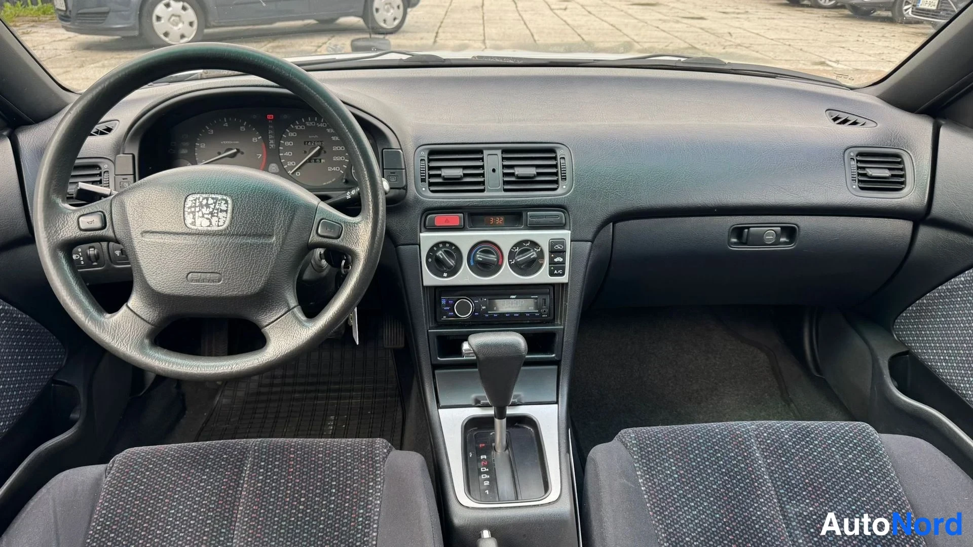 Muu: Ohjaamo eteenpäin kuvattuna: Honda-ohjauspyörä, mittaristo, automaattivaihteen valitsin, radiot ja ilmastointisäätimet näkyvät.