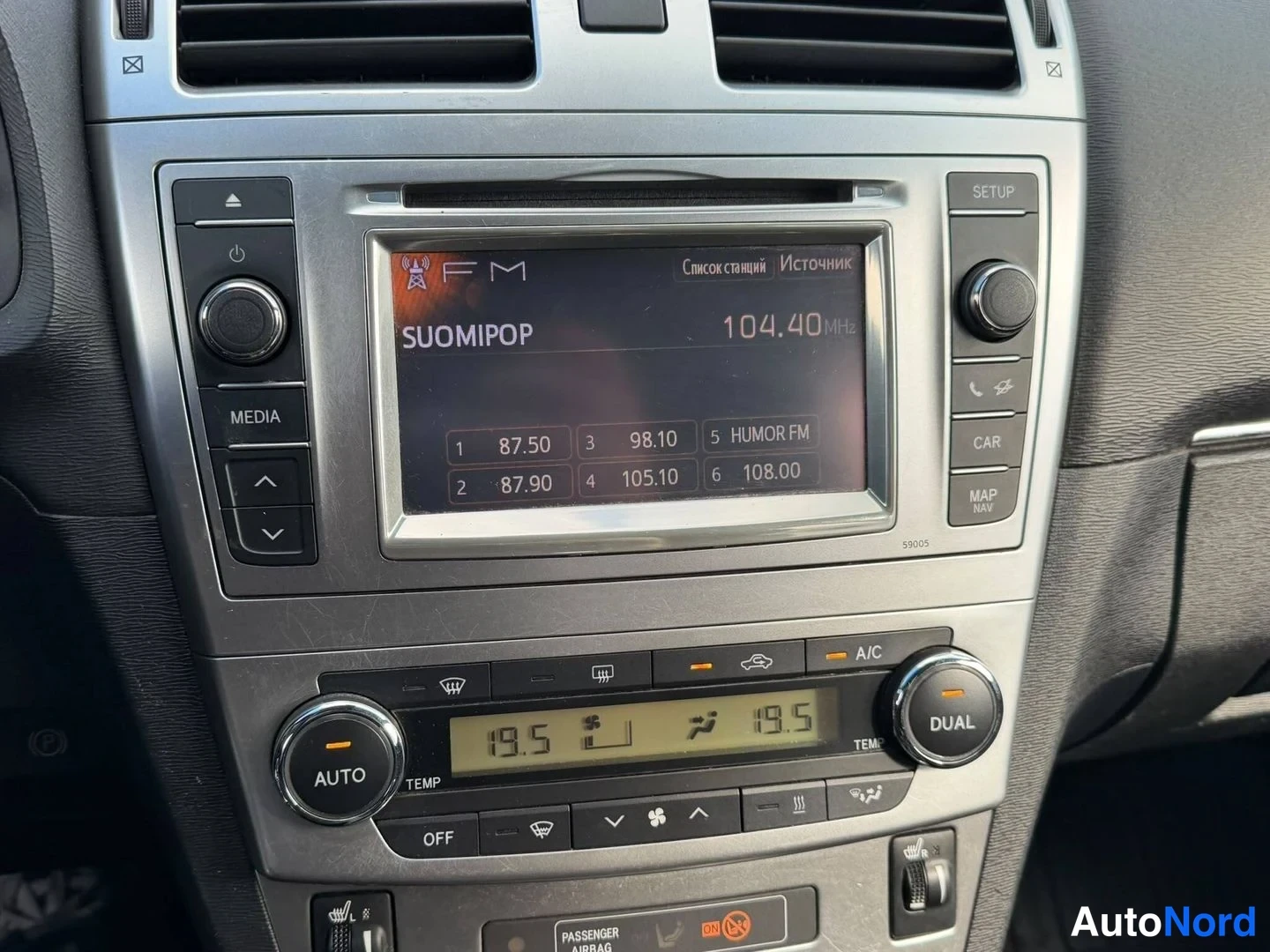 Yksityiskohta: Kojelaudan keskusn%C3%A4ytt%C3%B6 n%C3%A4ytt%C3%A4%C3%A4 FM-radioasemaa SUOMIPOP 104,40 MHz taajuudella; alla ilmastointipaneeli, jossa AUTO- ja DUAL-napit sek%