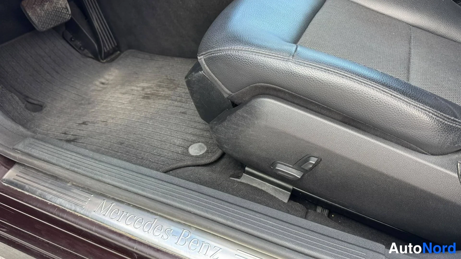 Sivulta: Kuljettajan tila: Mercedes-Benz-tekstillä varustettu oven kynnys, mattotepit ja sähköistuimen säätövipu.