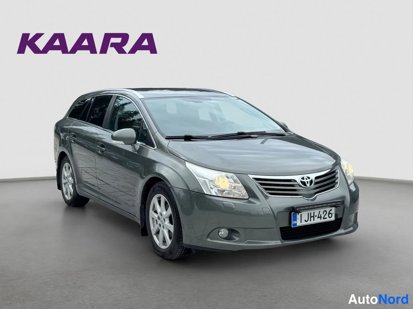 Etuviisto, nokka oikealle: Tummanharmaa Toyota Avensis -farmari etuviistosta oikealle, rekisteritunnus.