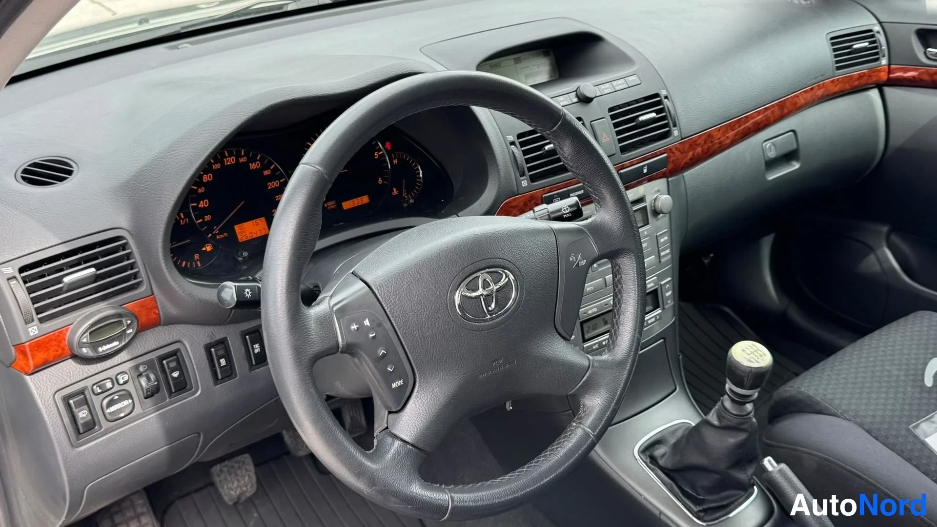 Muu: Toyota-ohjauspyörä, keskivarusteet ja manuaalivaihteen keppinappi näkyvät.