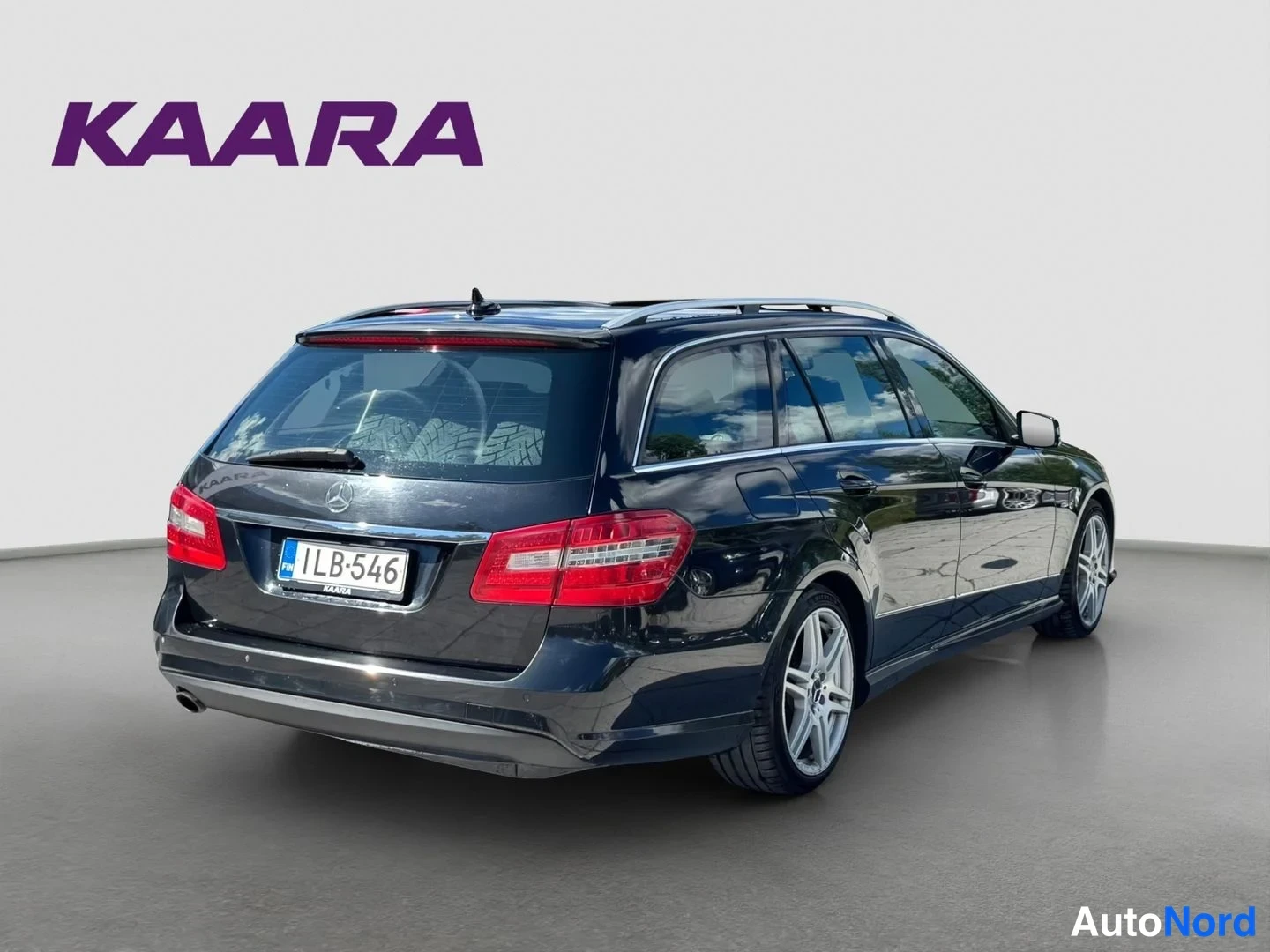 Takaviisto: Musta Mercedes-Benz farmari takaa vasemmalta kolmannesnäkymässä, rekisteritunnus, koristeet ja monivanteet.