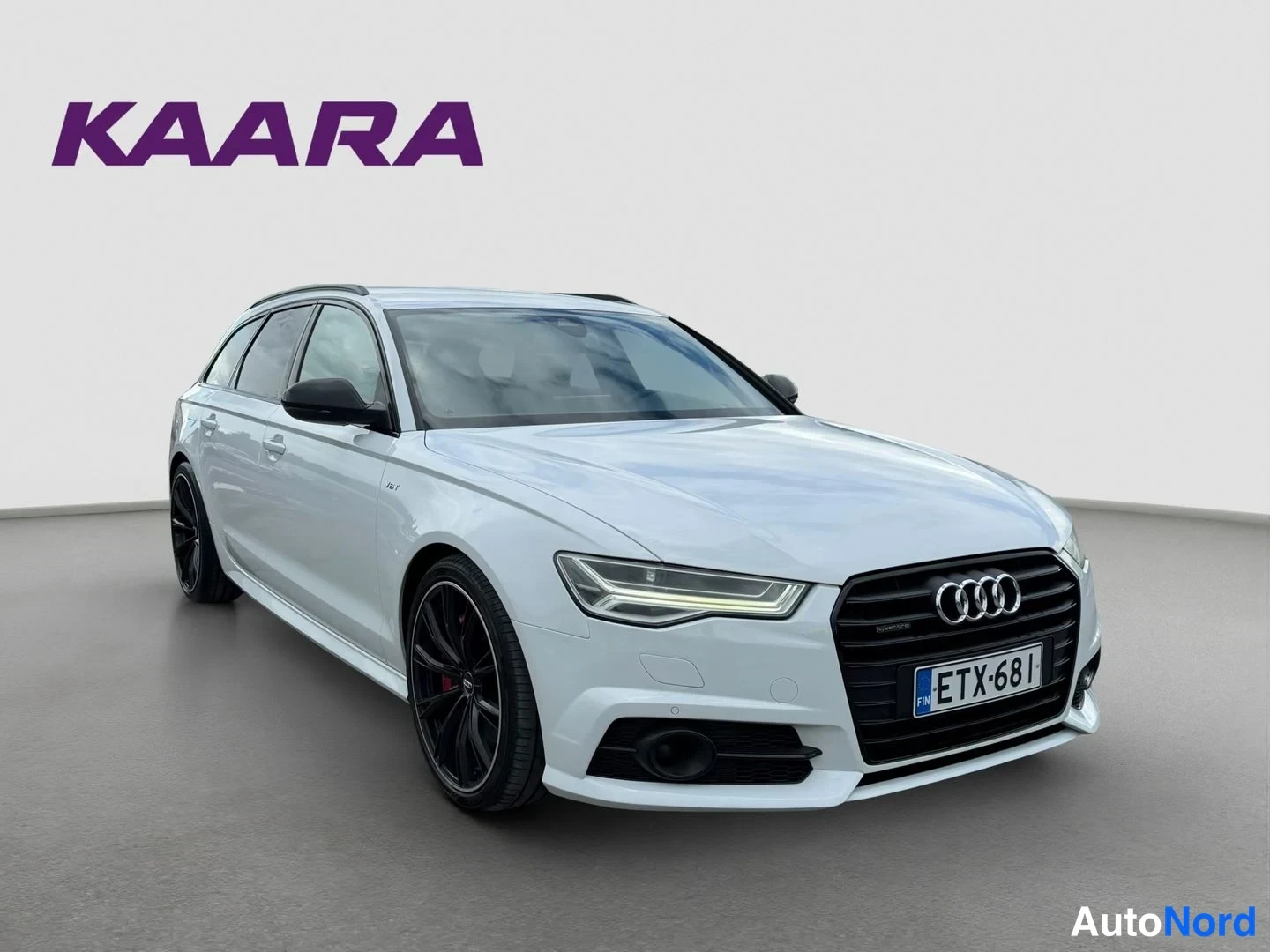 Etuviisto, nokka oikealle: Valkoinen Audi A6 Avant -farmari etukulmasta oikealle, mustat vanteet ja rekisteritunnus.