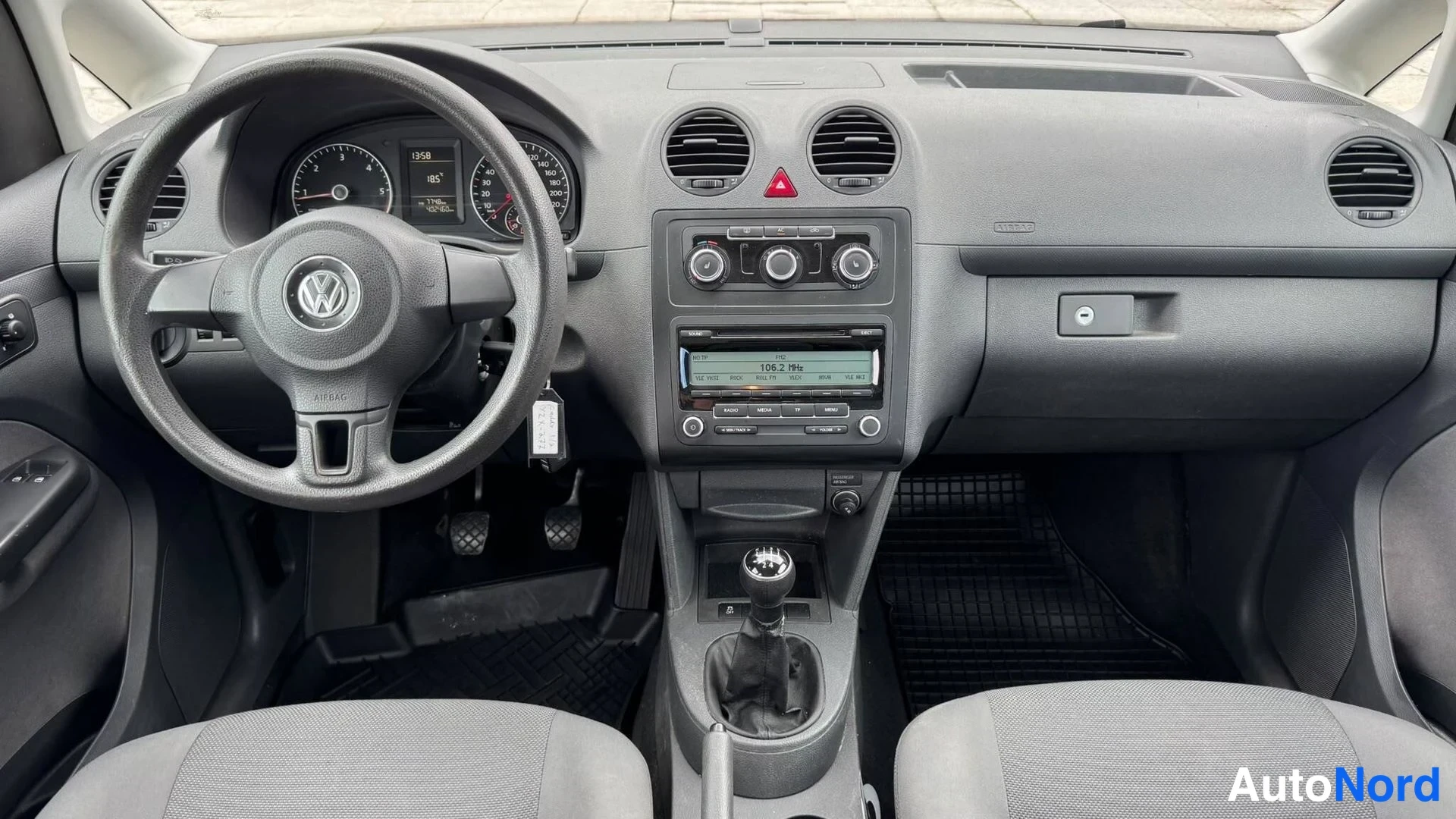 Yksityiskohta: Volkswagen Caddy -ohjaamo etupäin: ohjauspyörä, mittaristo, manuaalivaihteisto ja radio näytöllä 106.2 MHz