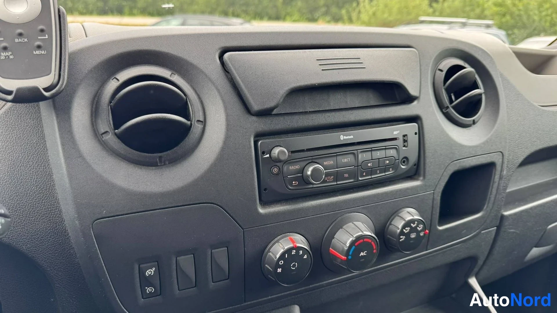 Sivulta: Tumma kojelaudan keskiosaan asennettu radio-CD-yksikkö Bluetooth-merkinnällä, kahdeksan pyöreää ilmastointisuutinta ja kolme nuppia, joissa AC-merkintä.