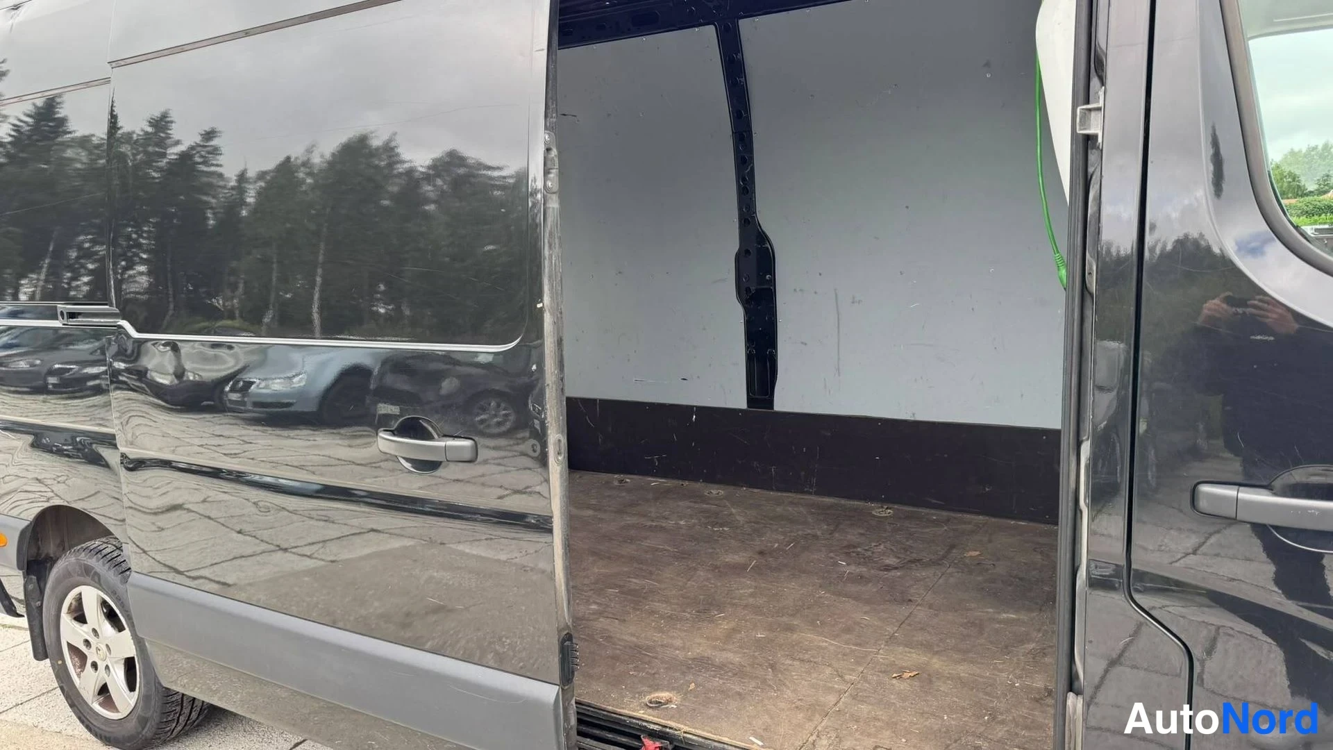 Muu: Mustan pakettiauton avattu sivuovi, tyhjä kuormatila ja osa kyljestä ja takarenkaasta näkyvissä.