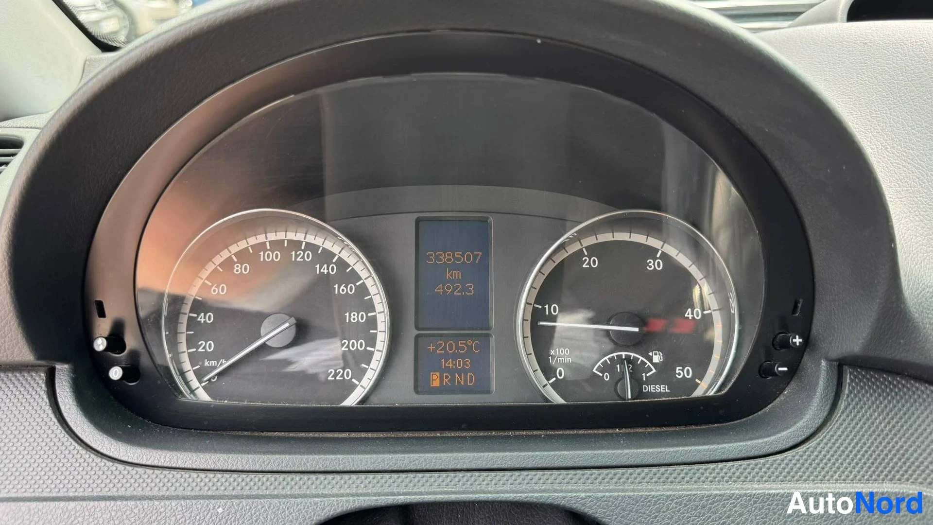 Yksityiskohta: Kojelaudan mittaristo: nopeusmittari, polttoainemittari ja näyttö, jossa lukee 338507 km sekä R-N-D -vaihdevalinnat.