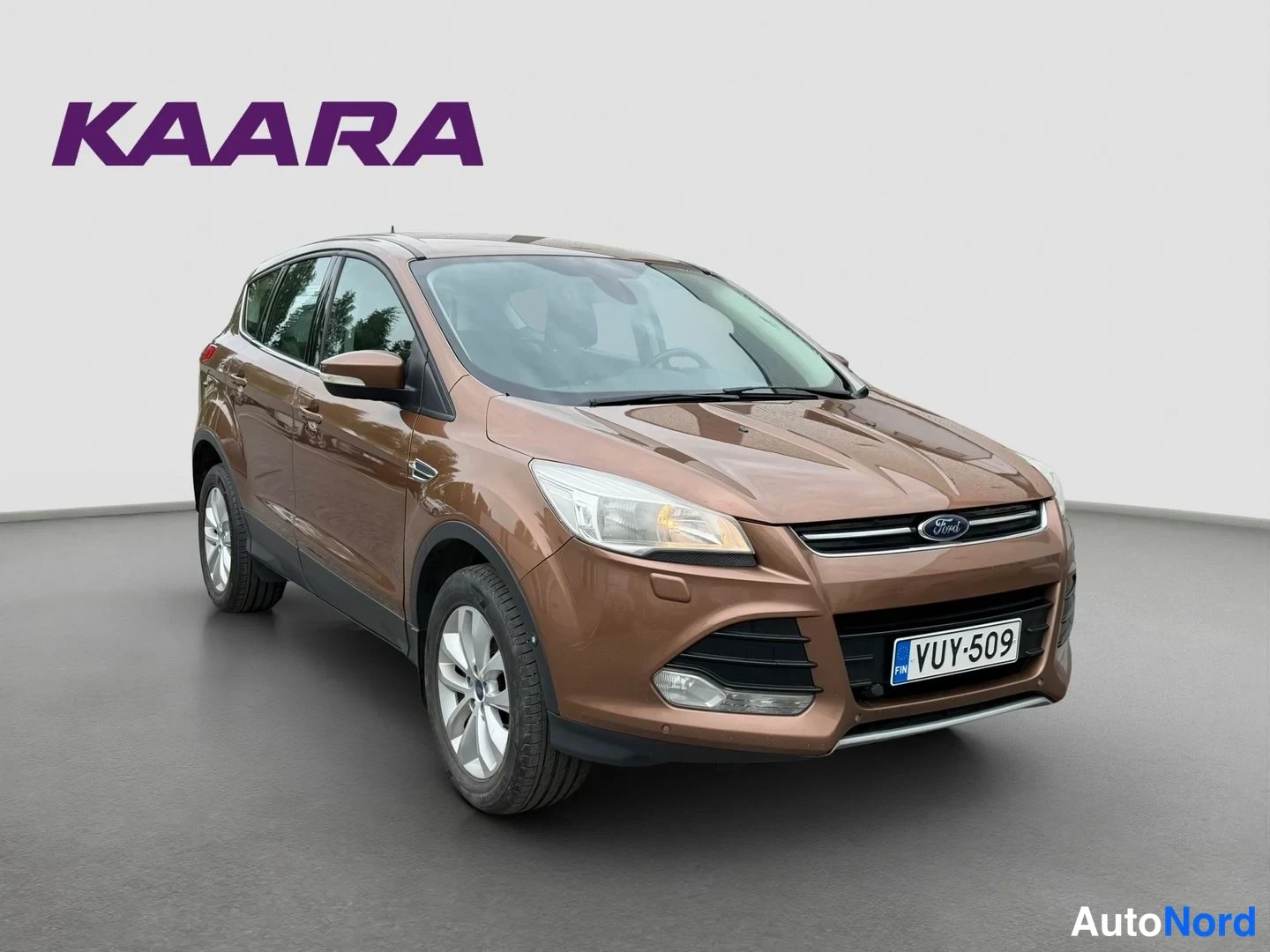 Etuviisto, nokka oikealle: Ruskea Ford Kuga etukulmasta oikealta kuvattuna, edessä Ford-merkki ja rekisteritunnus.