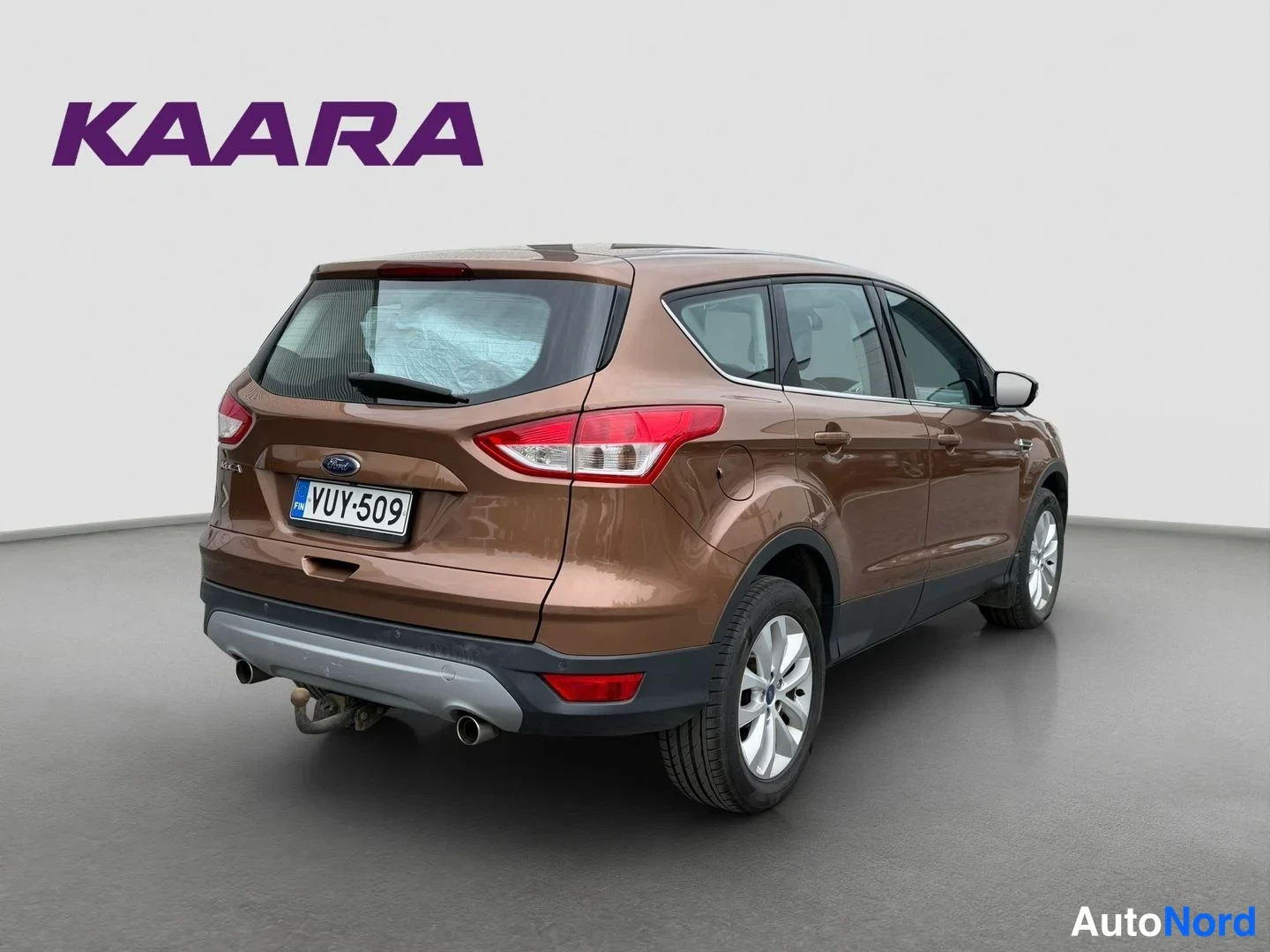 Takaviisto: Ruskea Ford Kuga takakulmasta vasemmalta kuvattuna, takana Ford-merkki, rekisteritunnus ja metallinen lentokoukun törmäyssuoja.