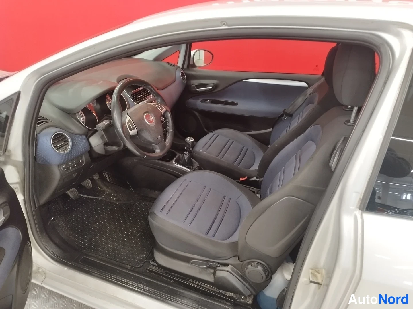 Muu: Fiat Punto Evo:n matkustamo ovista katsottuna: tummansiniset kangasistuimet, Fiat-ohjauspyörä, käsivaihteisto ja kojelauta sinisin detaljein.