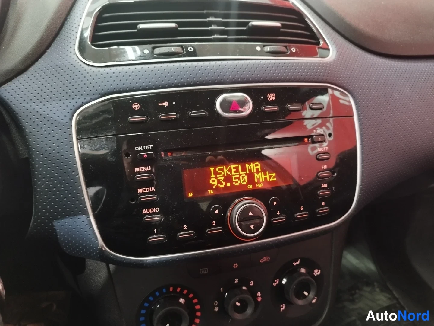 Muu: Kojelaudan keskusradio: näytössä teksti ISKELMA 93.50 MHz, CD-slot ja radiopainikkeet sekä alla lämmitys- ja ilmastointisäätimet.