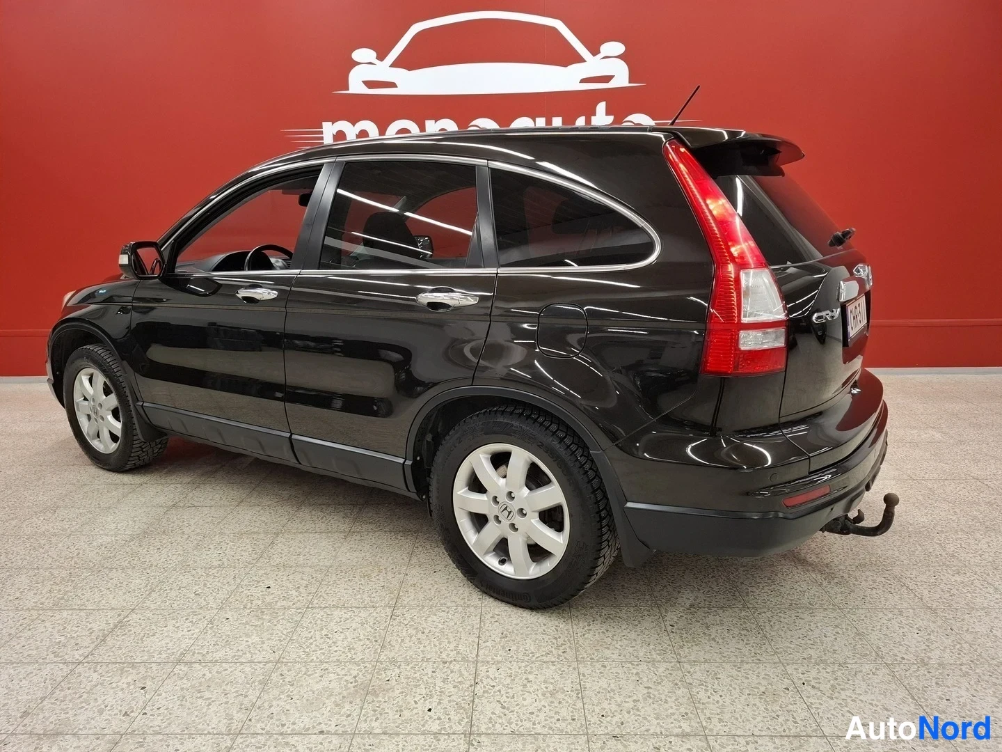 Takaviisto: Mustan Honda CR-V:n takakulmakuva vasemmalta, perävasen ja takapyörä näkyvissä punaisella taustalla.