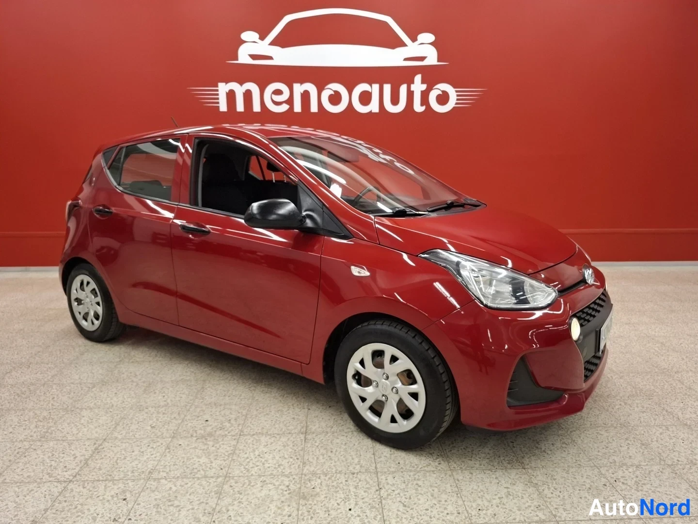 Etuviisto, nokka oikealle: Hyundai i10 -viistotakaa-etuviisto, punainen koripinta, asemoitu myyjän tiloissa.